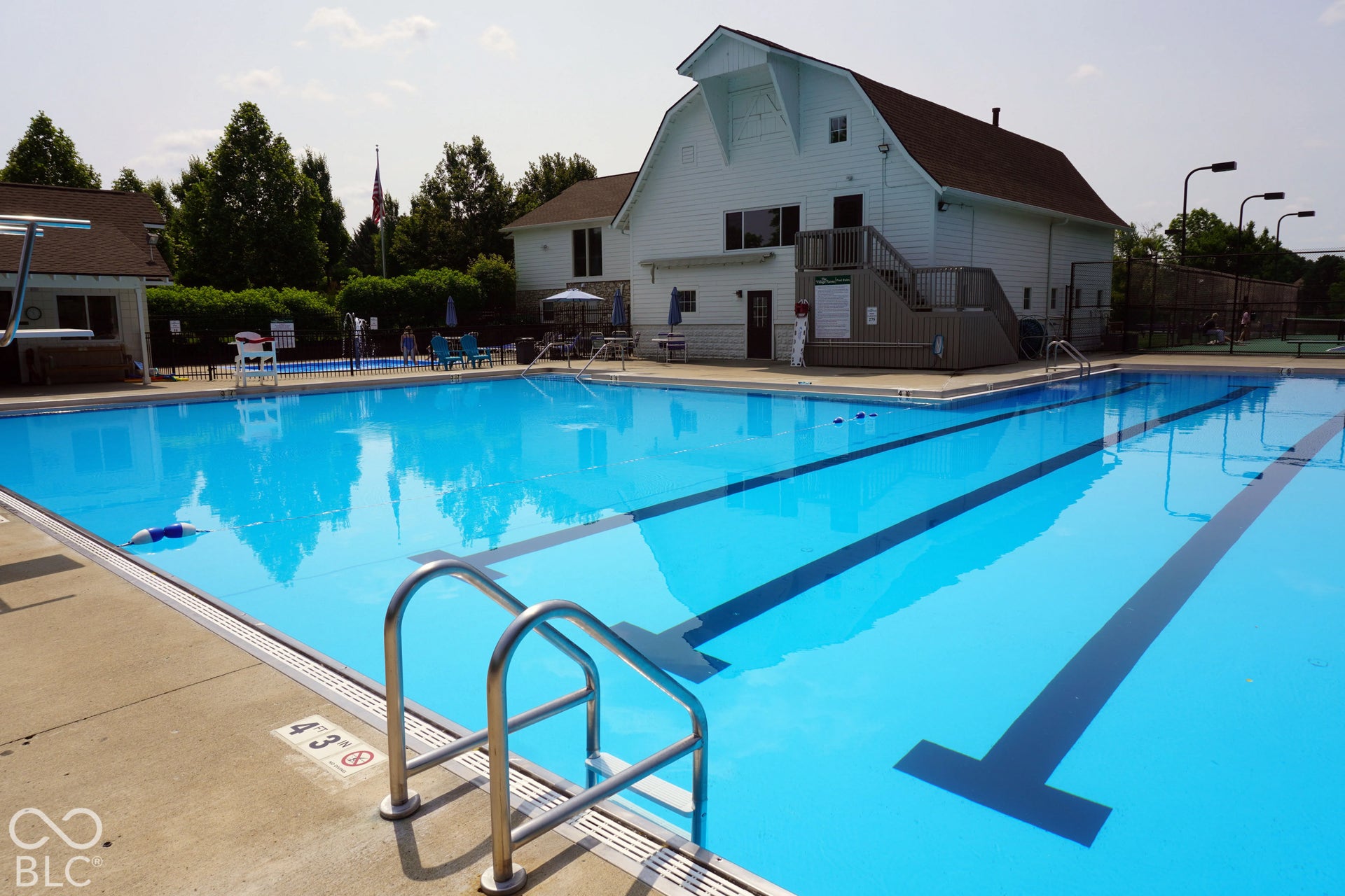 Expansive outdoor pool with lane lines and concrete decking, featuring a diving board and stainless steel pool ladders