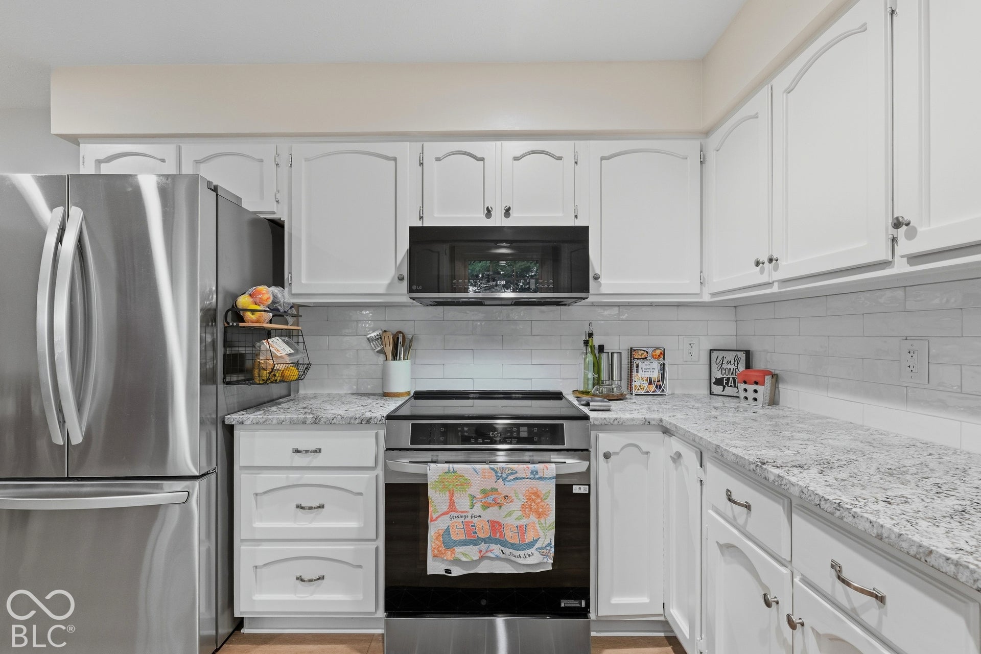 Stainless steel appliances, white cabinetry, subway tile backsplash, and light-toned countertops