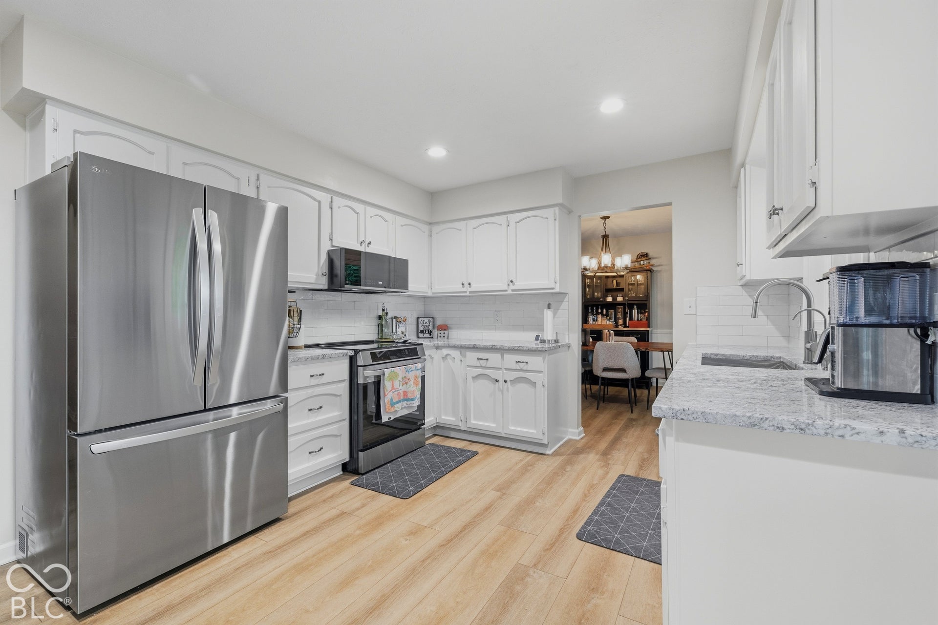 Stainless steel appliances, white cabinetry, light wood-finish flooring, white subway tile backsplash, and light-toned countertops