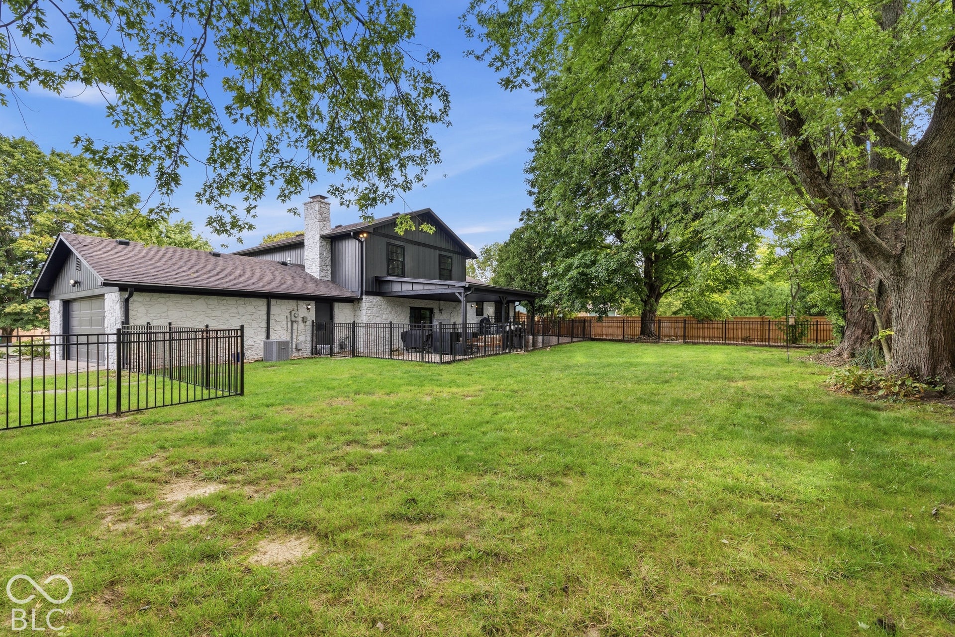 Expansive grassy yard with mature trees, a black metal fence, and a wooden privacy fence