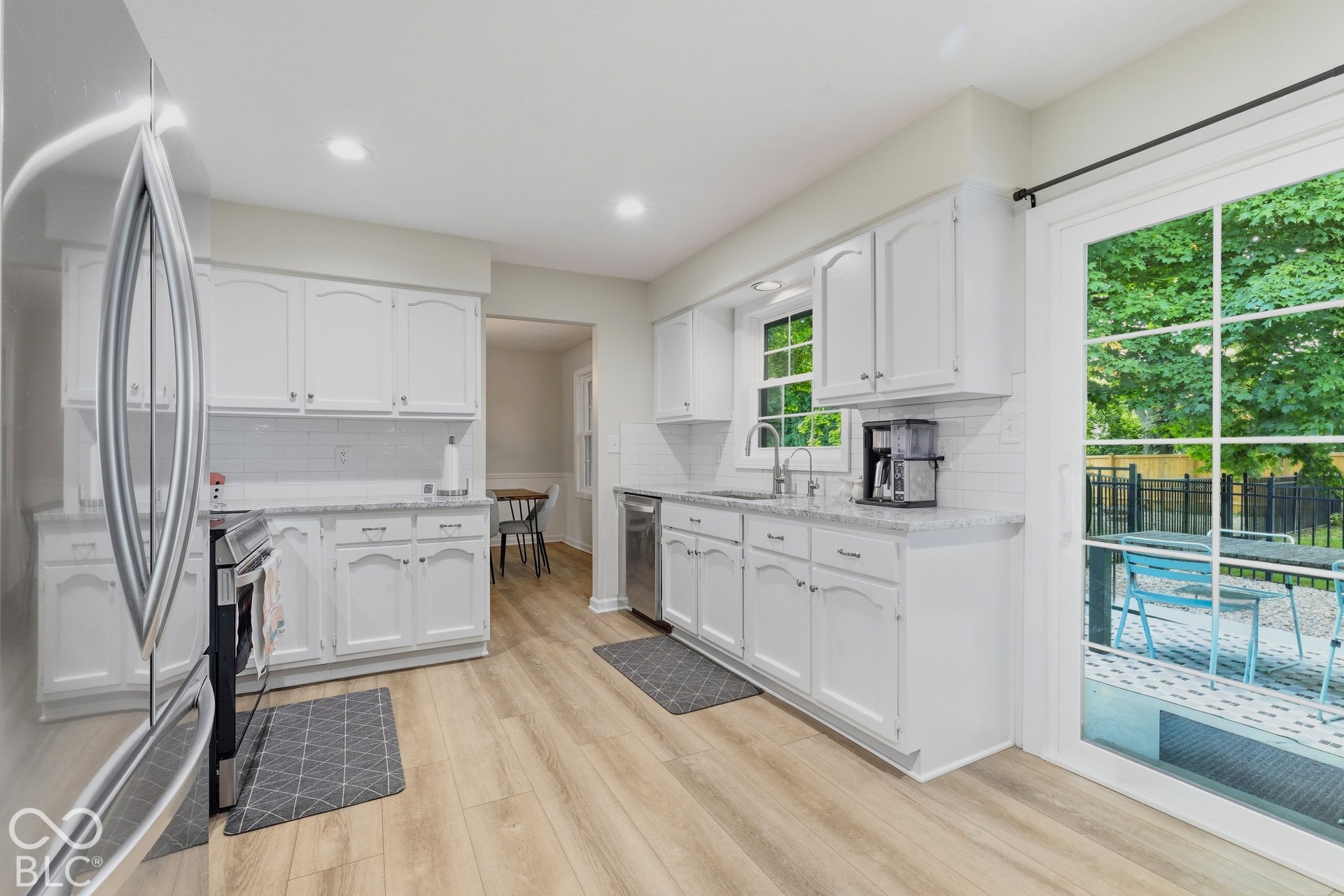 White cabinetry with matching backsplash, stainless steel appliances, light wood-finish flooring, and white countertops