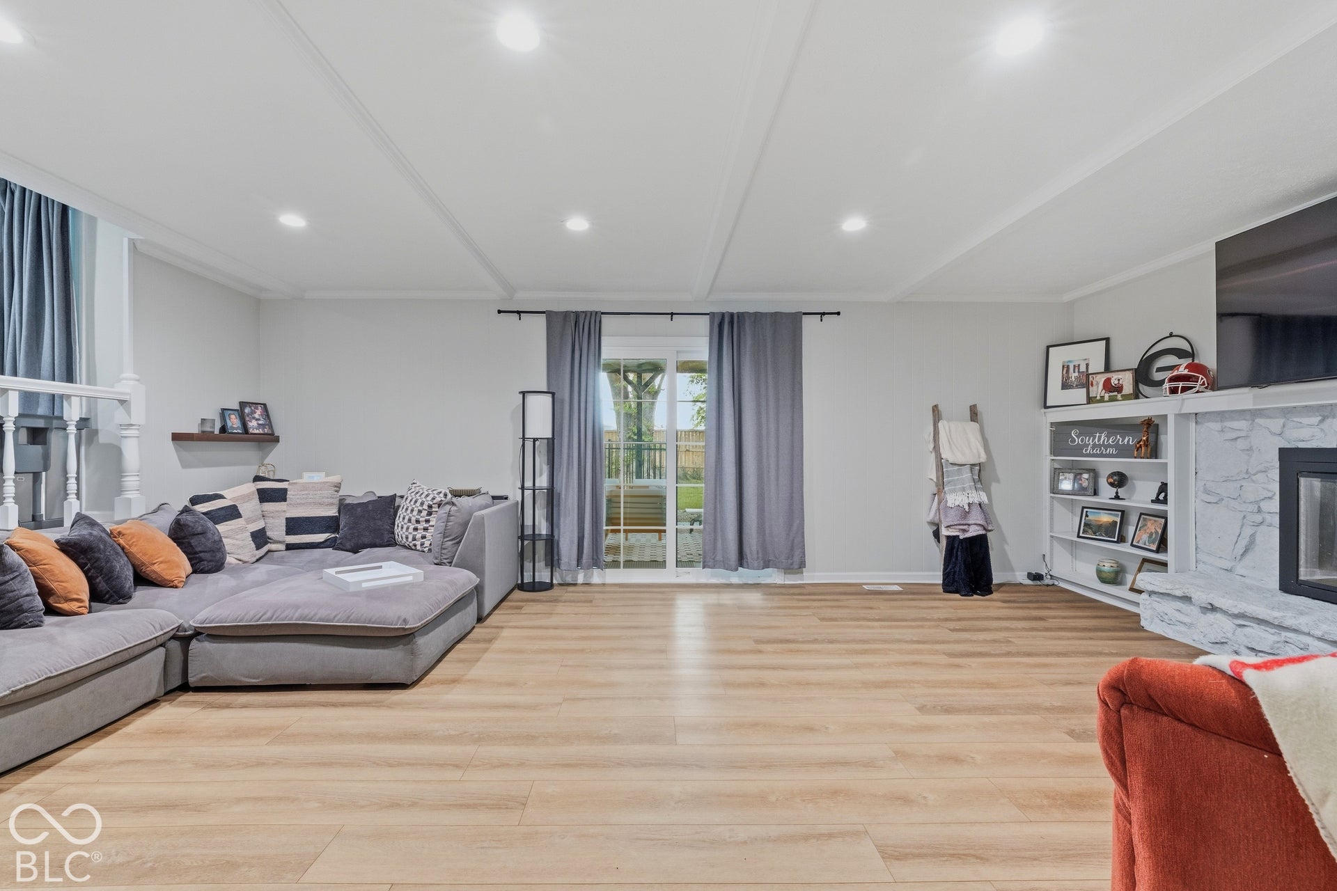 Recessed lighting, wood-finish flooring, white built-in shelving, stone fireplace surround, and sliding glass door