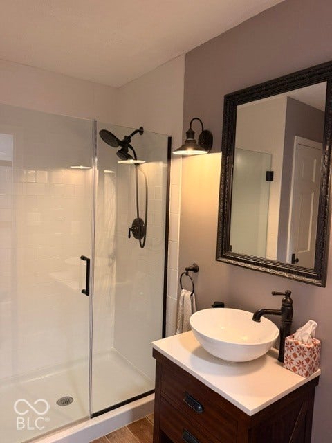 Glass-enclosed shower with subway tile surround, dark bronze fixtures, framed mirror, vessel sink, and wood-finish vanity with countertop