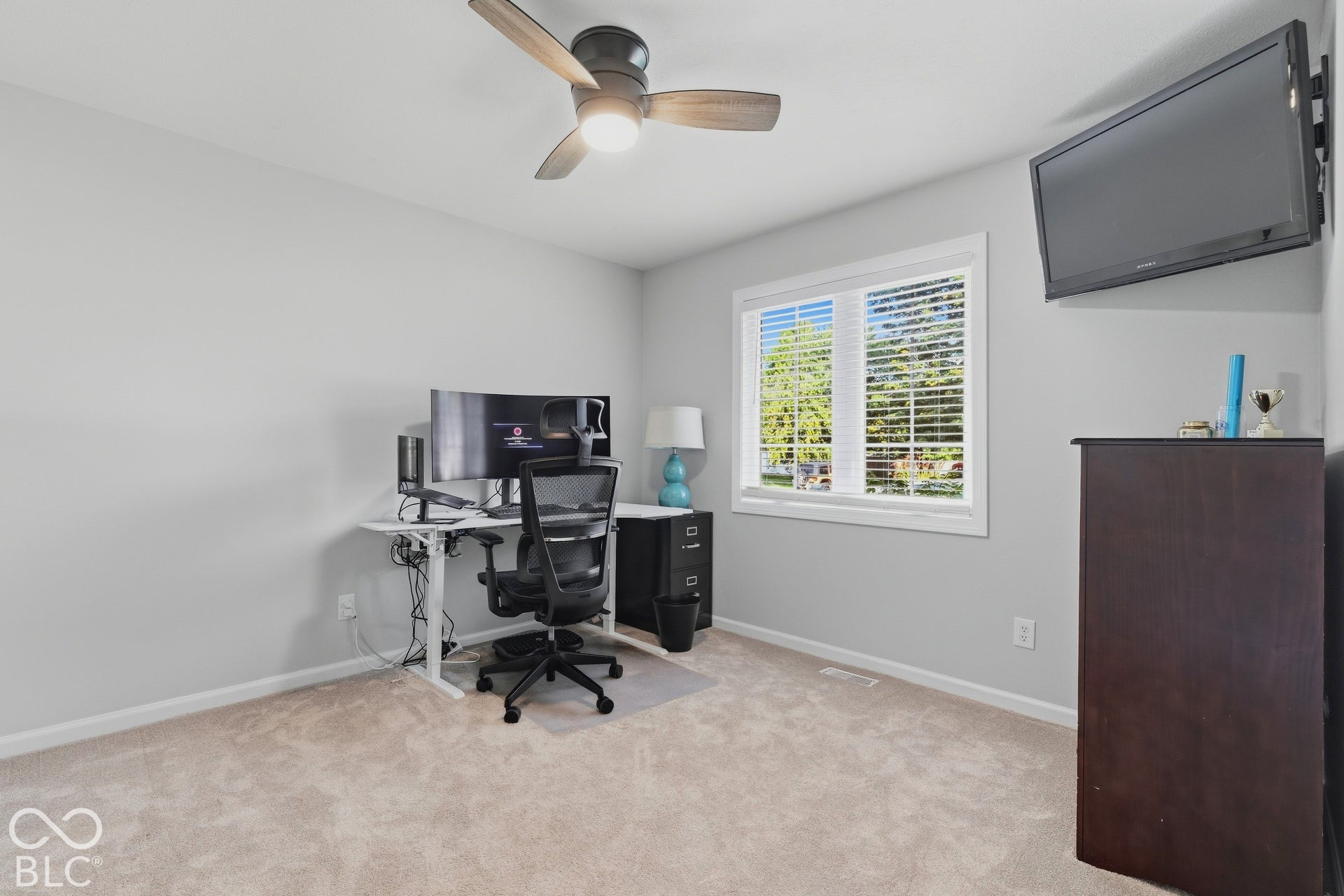 Neutral-toned wall-to-wall carpeting, ceiling fan with integrated lighting, and a single window with blinds