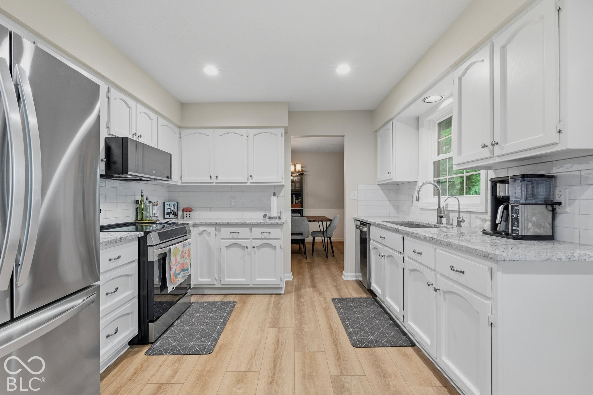 Kitchen featuring wood-finish flooring, white cabinetry with silver-tone hardware, a stainless steel refrigerator, white subway tile backsplash, and light-colored countertops