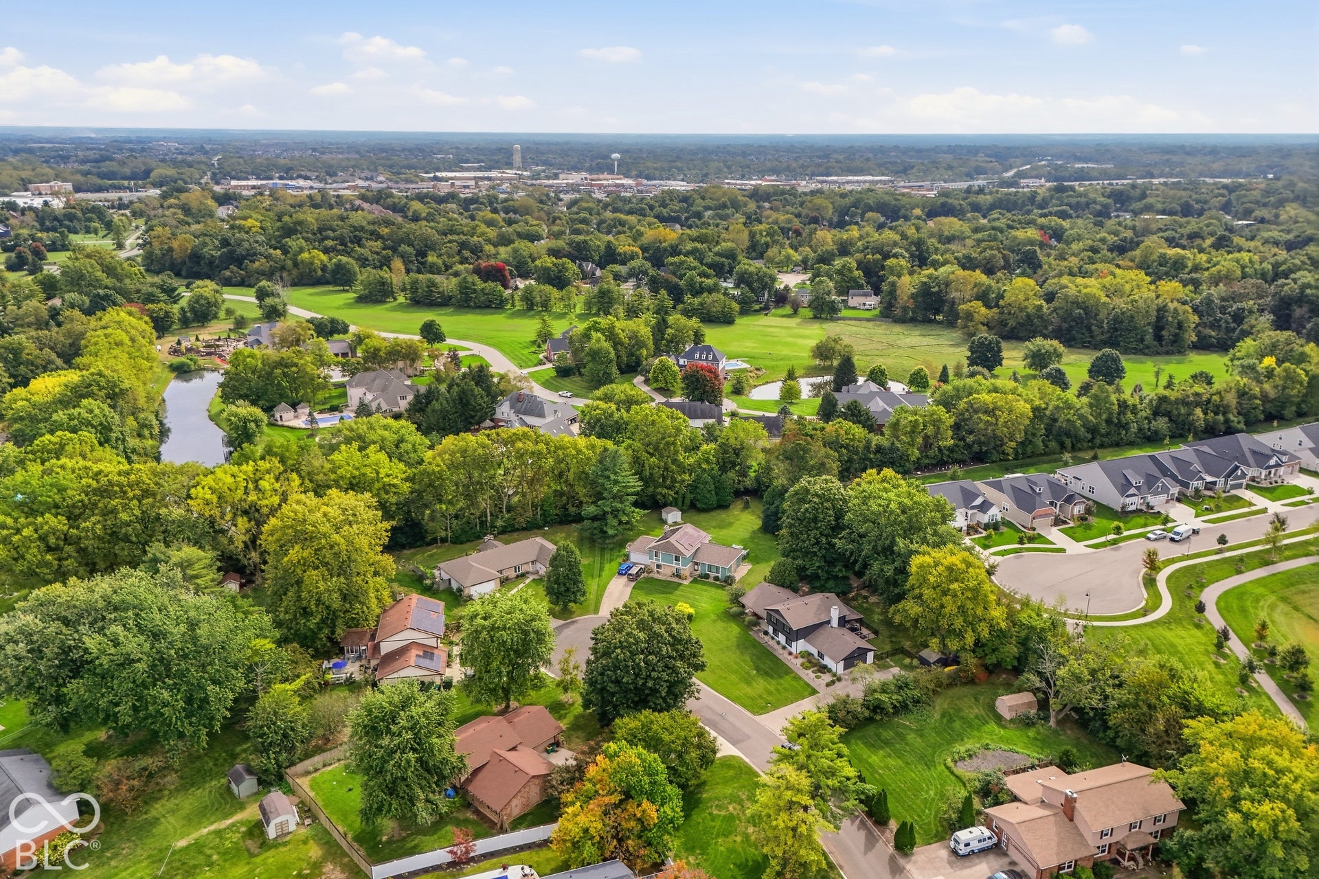 Aerial perspective of a residential area with varied housing styles, mature trees, and a body of water