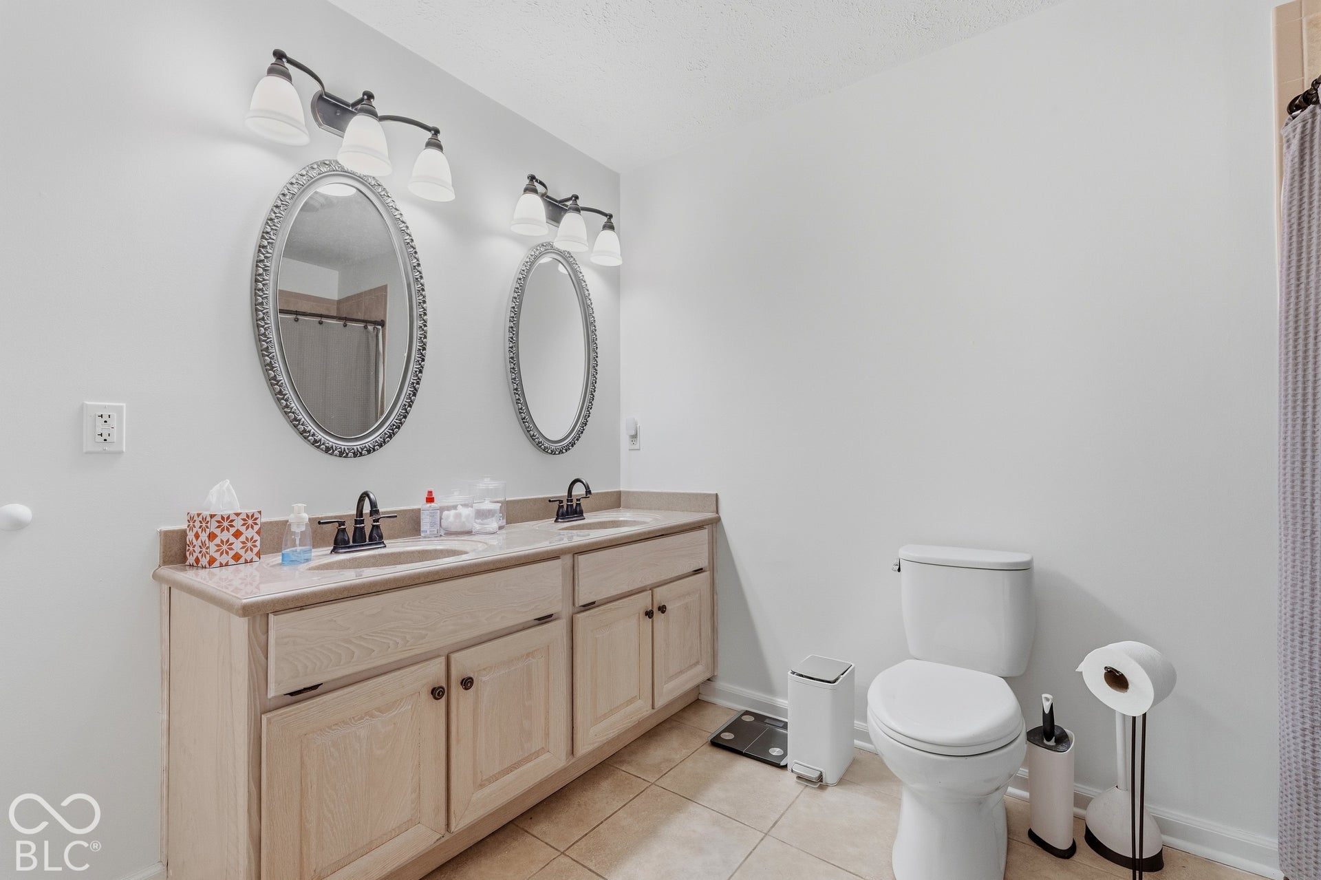 Dual vanity with light wood-finish cabinetry and undermount sinks, flanked by oval mirrors