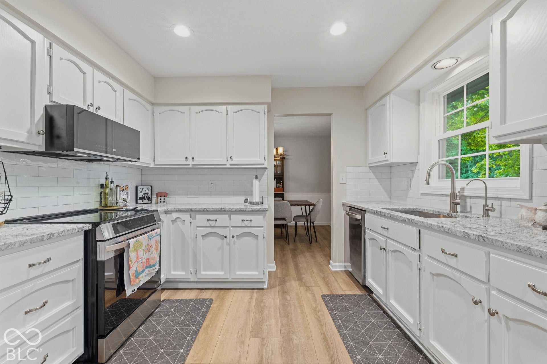 White cabinetry, subway tile backsplash, light-toned wood-finish flooring, stainless steel appliances, and a window with natural light