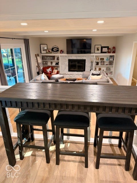 Recessed lighting, light wood-finish flooring, built-in shelving, stone-surround fireplace, and glass French doors to the exterior