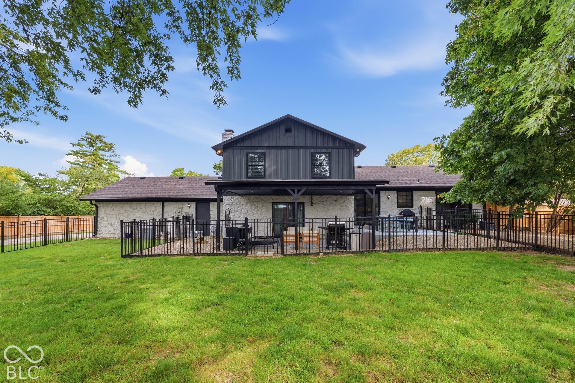 Expansive lawn area with a black metal fence enclosing a patio space, a dark-toned two-story exterior, and a single-story wing with light-colored textured siding