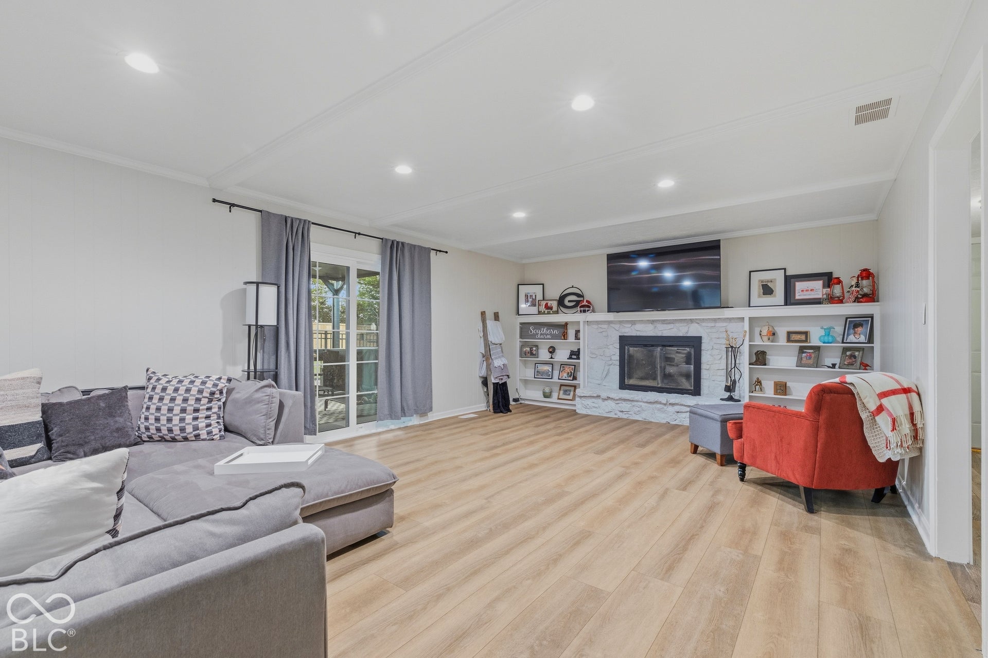 Wood-finish flooring throughout, featuring recessed lighting, a built-in fireplace with a stone surround, and integrated shelving