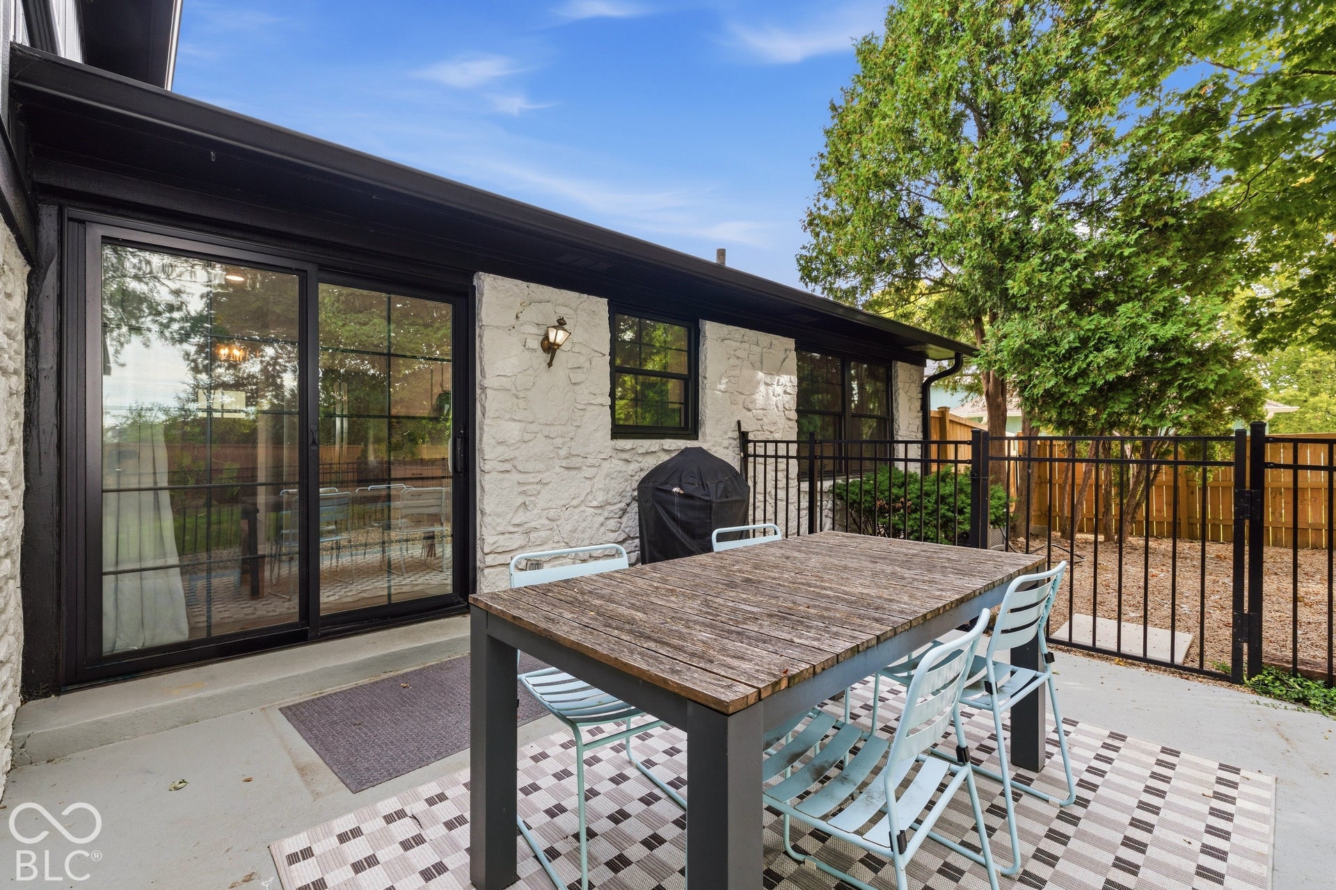 Exterior featuring white stone siding, black-framed sliding glass doors, black rain gutters, and a black metal fence
