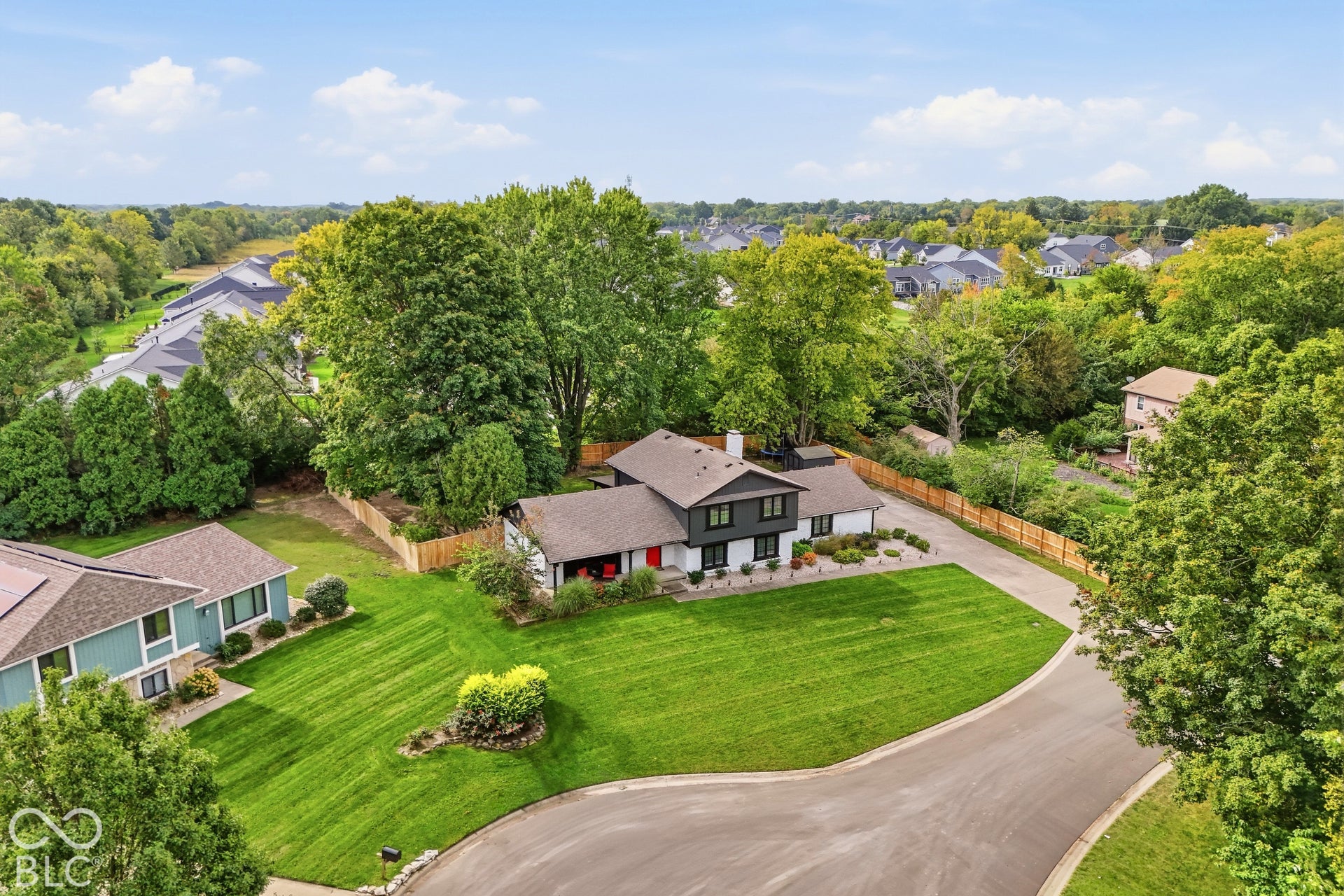 Modern exterior with a detached garage, expansive front lawn, paved driveway, and mature landscaping