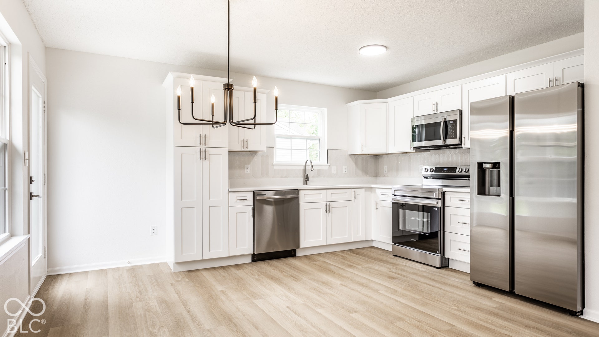 Kitchen featuring white shaker cabinetry, stainless steel appliances, wood-finish flooring, a white subway tile backsplash, and a modern black chandelier