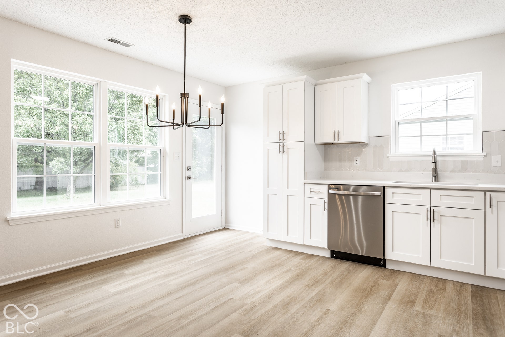 White shaker cabinetry with modern hardware, stainless steel dishwasher, and a single basin sink with a high-arch faucet