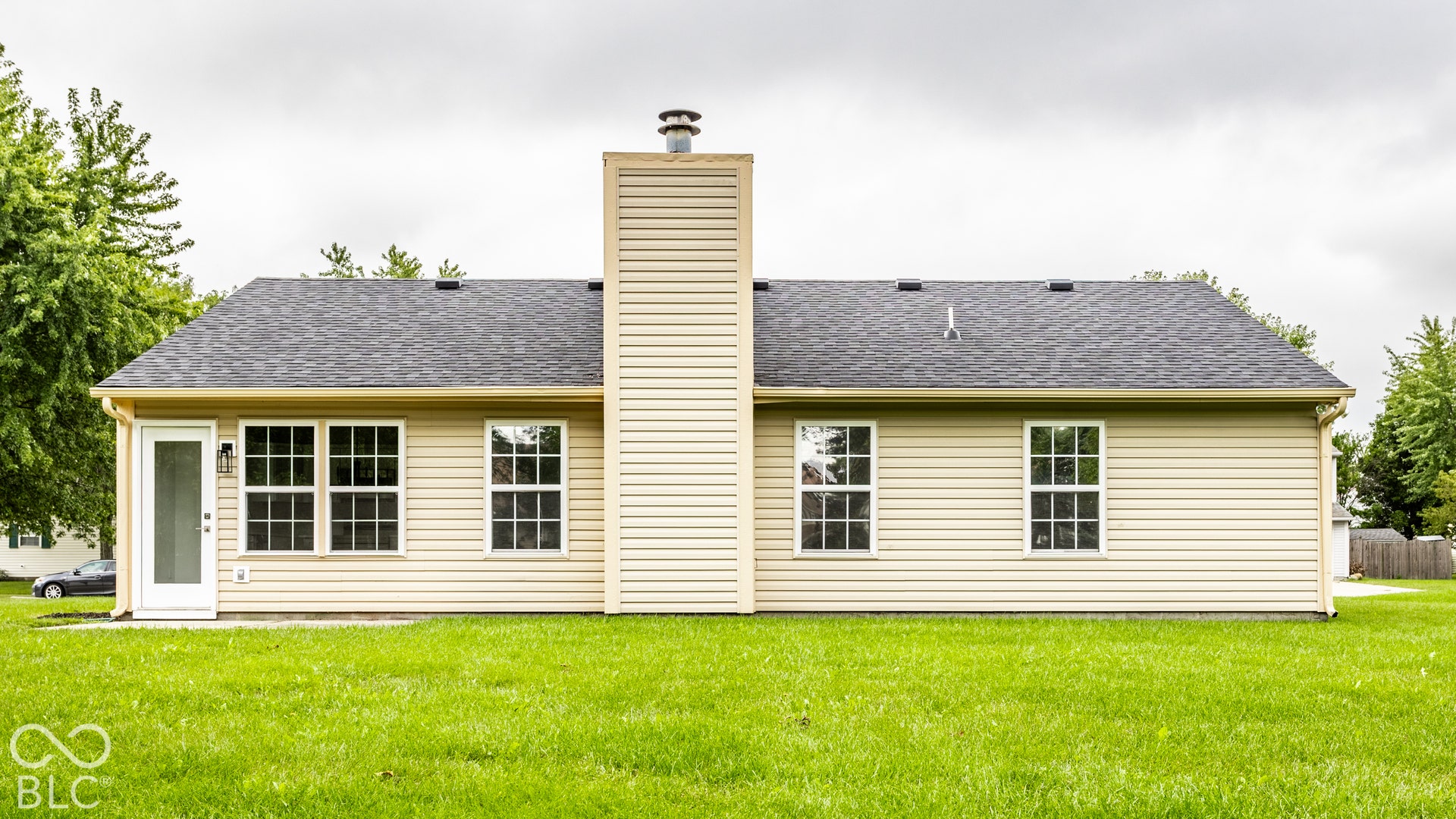Charming single-story residence featuring cream vinyl siding, a prominent central chimney, and a composition shingle roof
