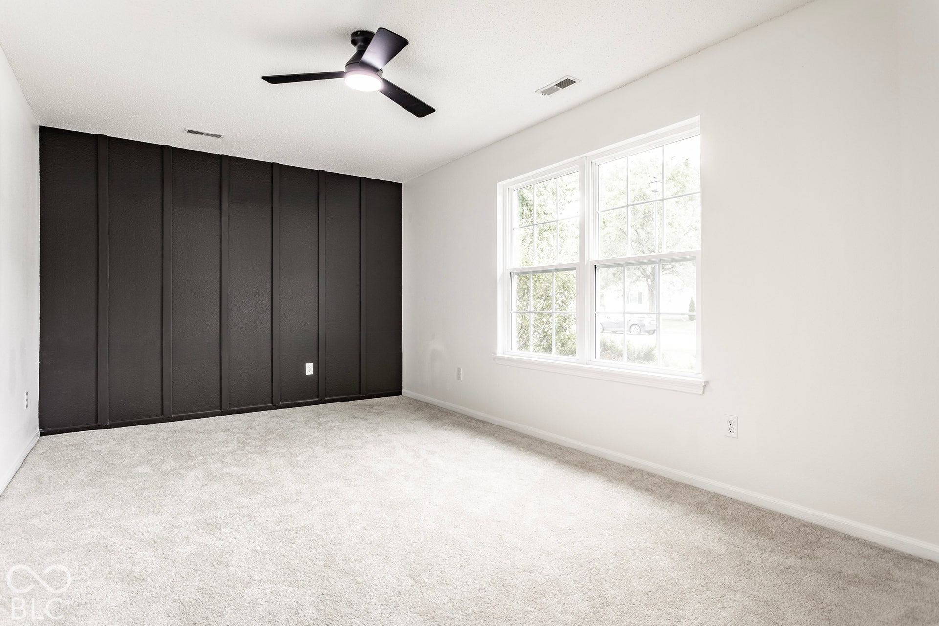 Spacious room featuring a decorative accent wall, two large windows, a ceiling fan, and light-toned carpeting