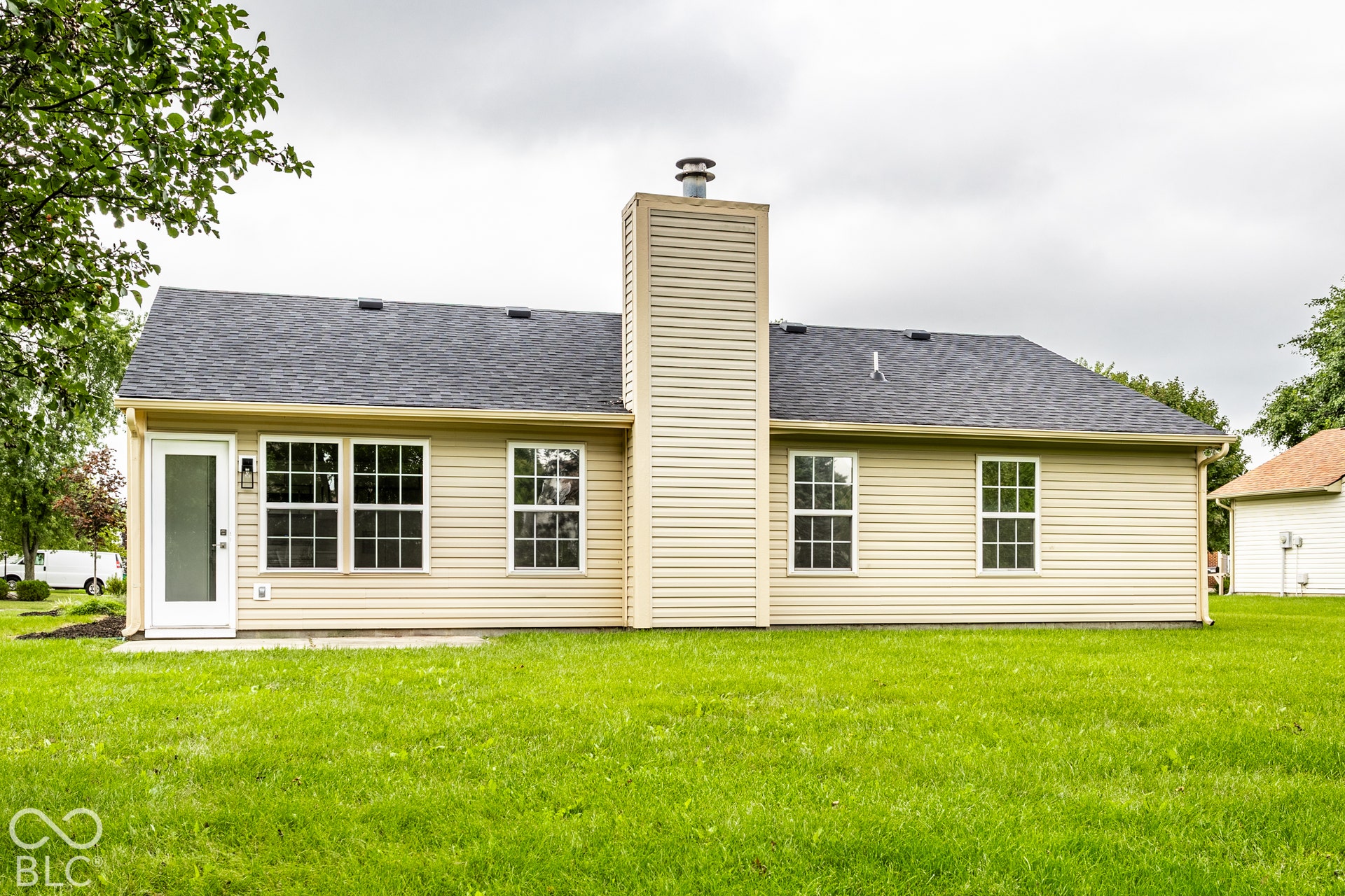 Exterior featuring light-colored siding, a dark shingle roof, a prominent chimney, multiple windows, and a glass-paneled door