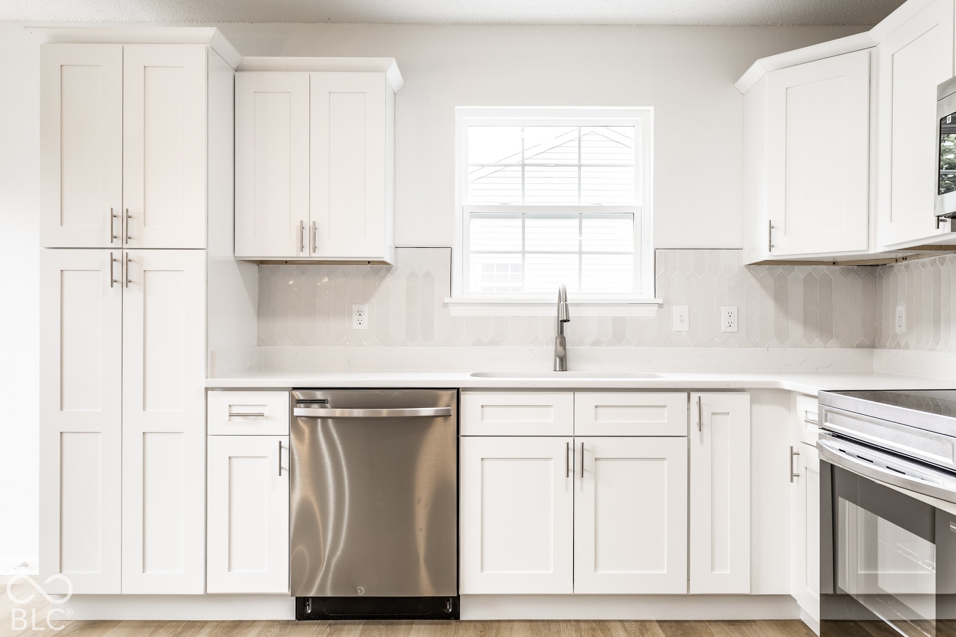 White shaker cabinetry, light-toned countertops, stainless steel appliances, and wood-finish flooring