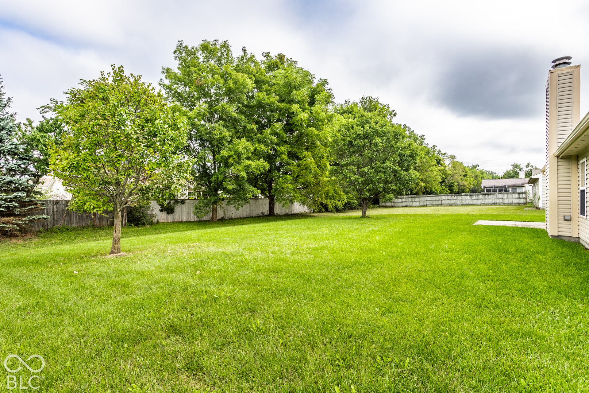 Expansive grass lawn with mature trees and a privacy fence