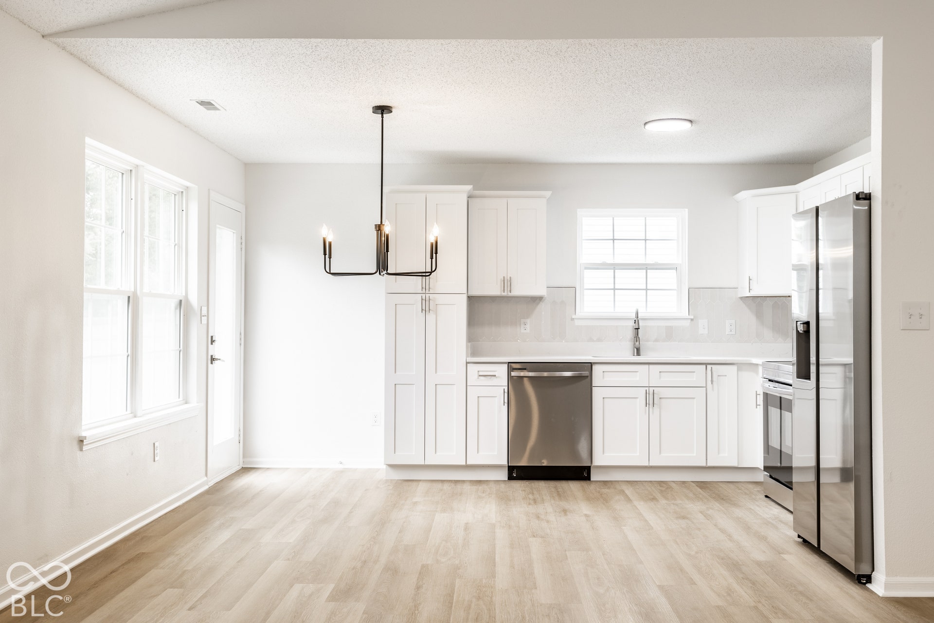 Open-concept kitchen and dining area featuring white cabinetry, stainless steel appliances, wood-finish flooring, and a contemporary chandelier