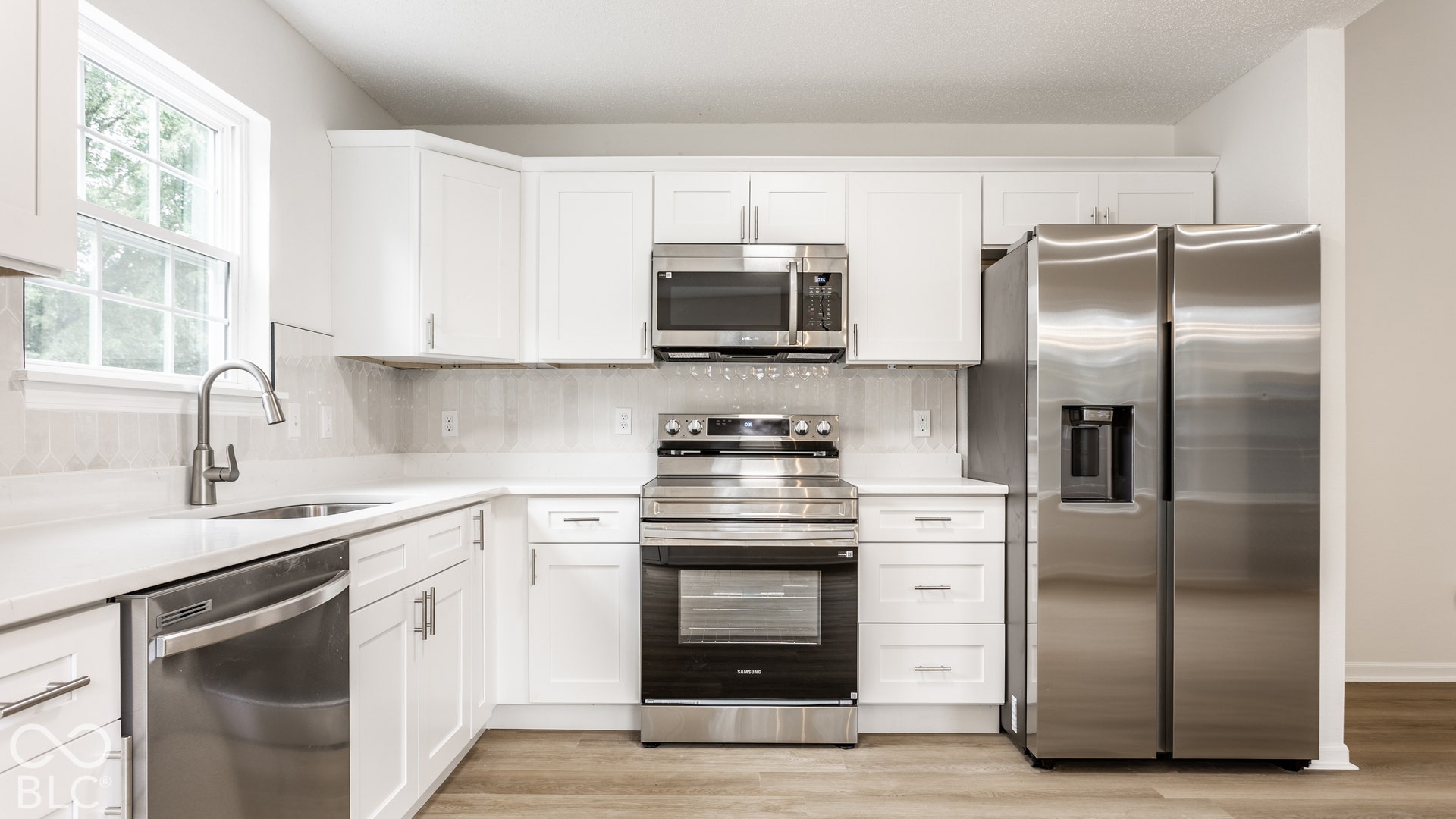 White shaker-style cabinetry, stainless steel appliances, light-toned countertops, and wood-finish flooring