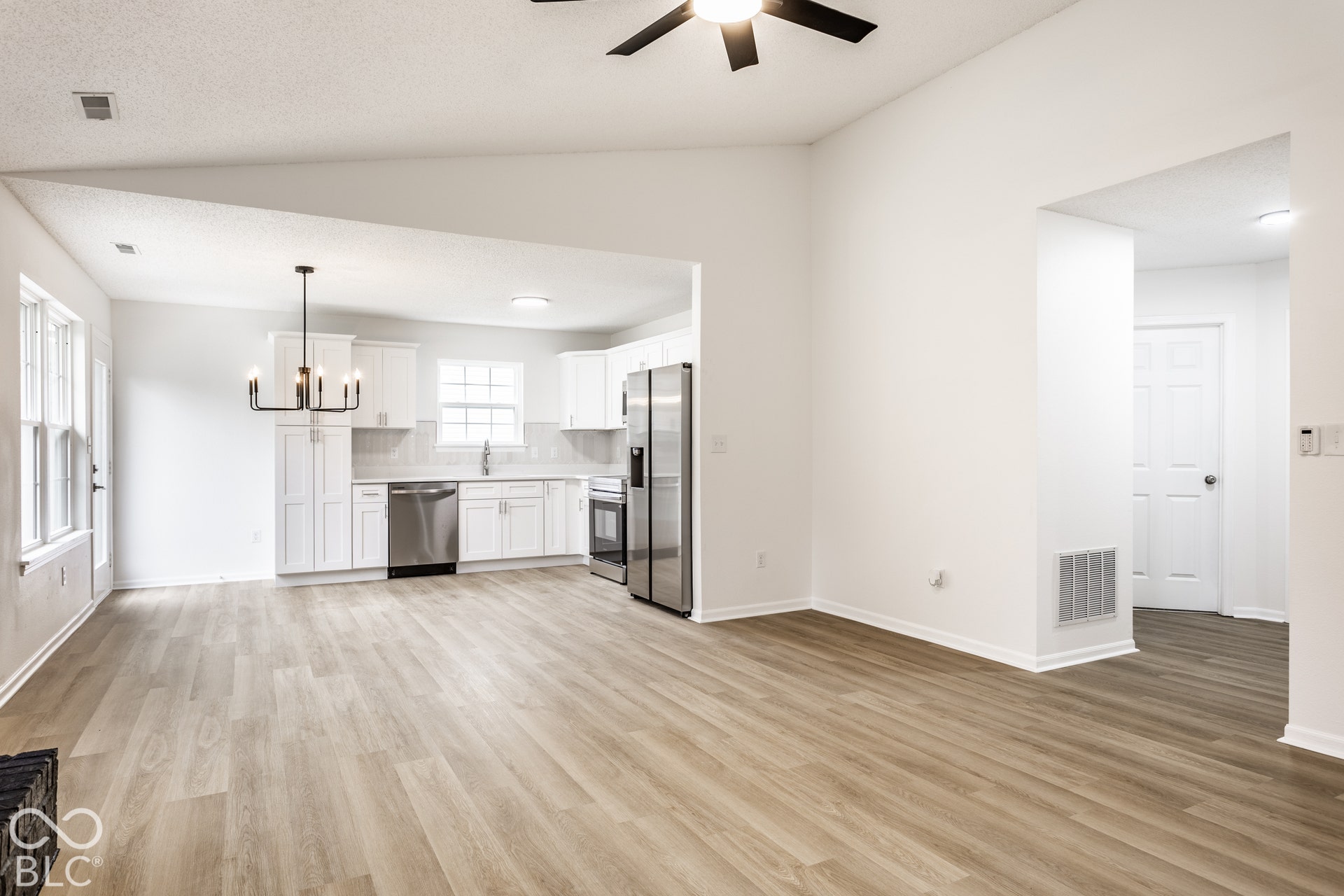 Vaulted ceilings, wood-finish flooring, white shaker cabinetry, stainless steel appliances, and a modern chandelier