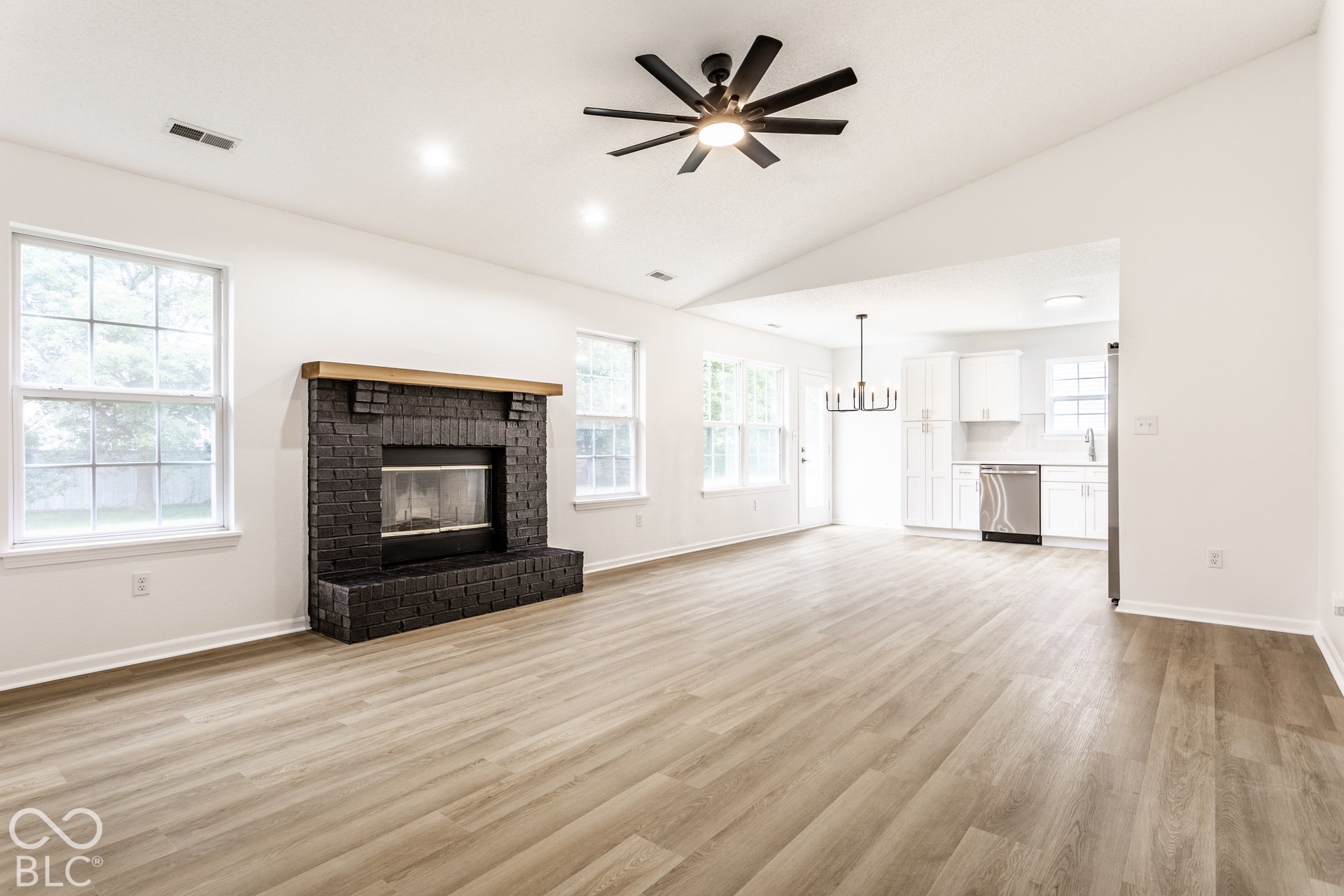Spacious room with wood-finish flooring, a black brick fireplace with a wood mantel, and multiple windows
