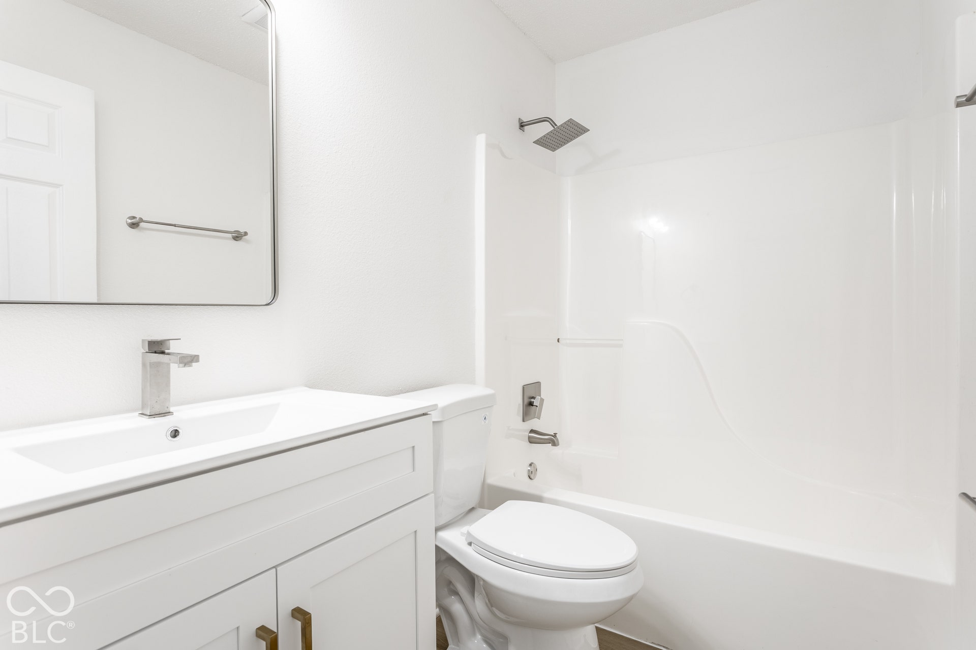 Vanity with integrated sink, rectangular mirror, brushed nickel faucet, and a white bathtub with an integrated shower