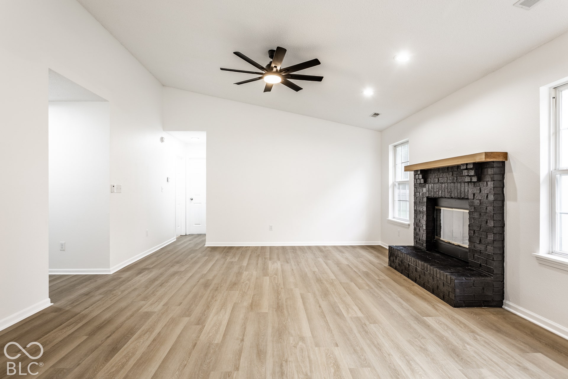 Vaulted ceiling with a ceiling fan, recessed lighting, wood-finish flooring, and a brick-finish fireplace with a wood mantle