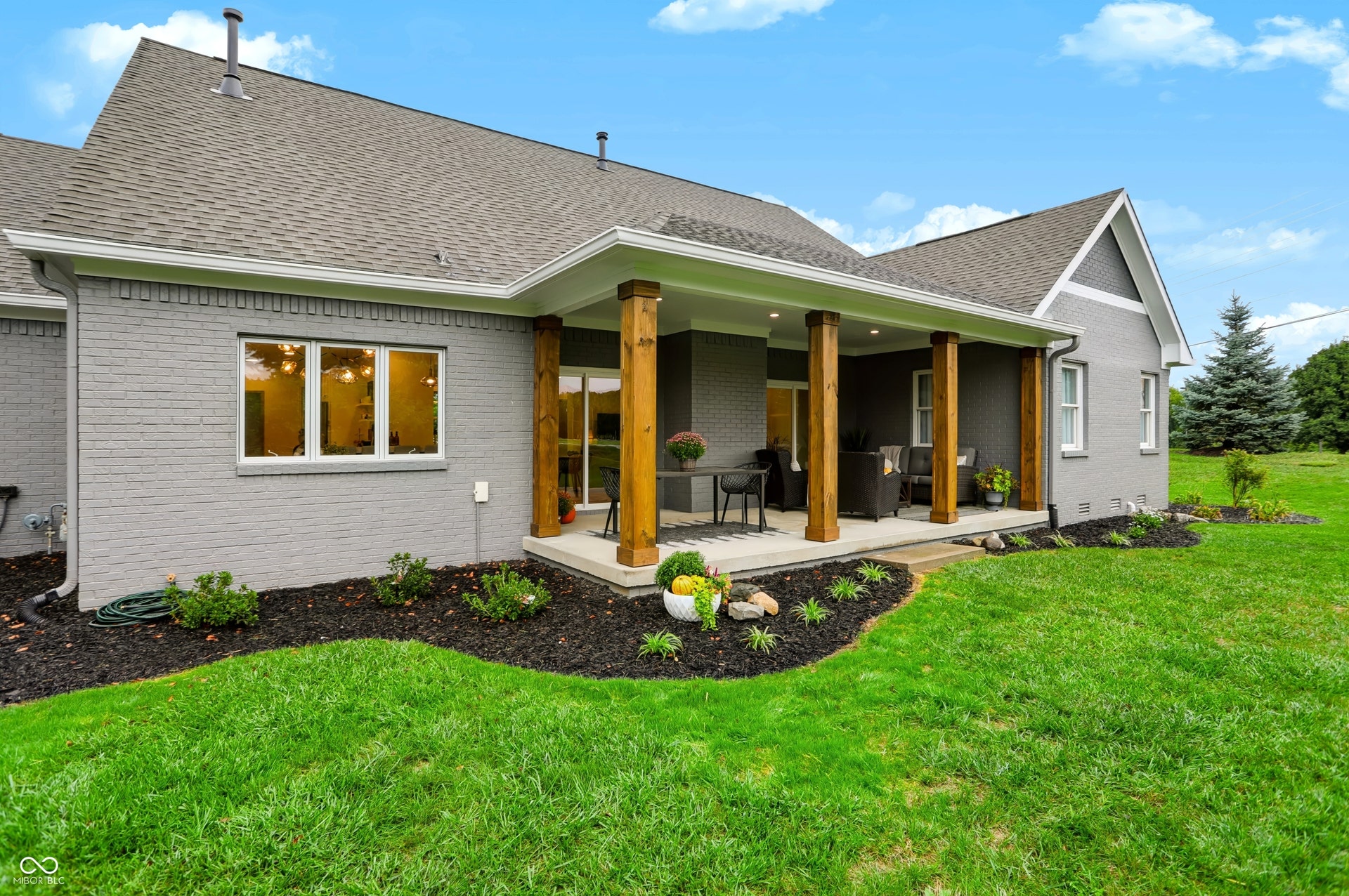 7405 Rooses Drive, Indianapolis, IN 46217 Expansive covered patio with natural wood columns, surrounded by manicured landscaping and a lush lawn