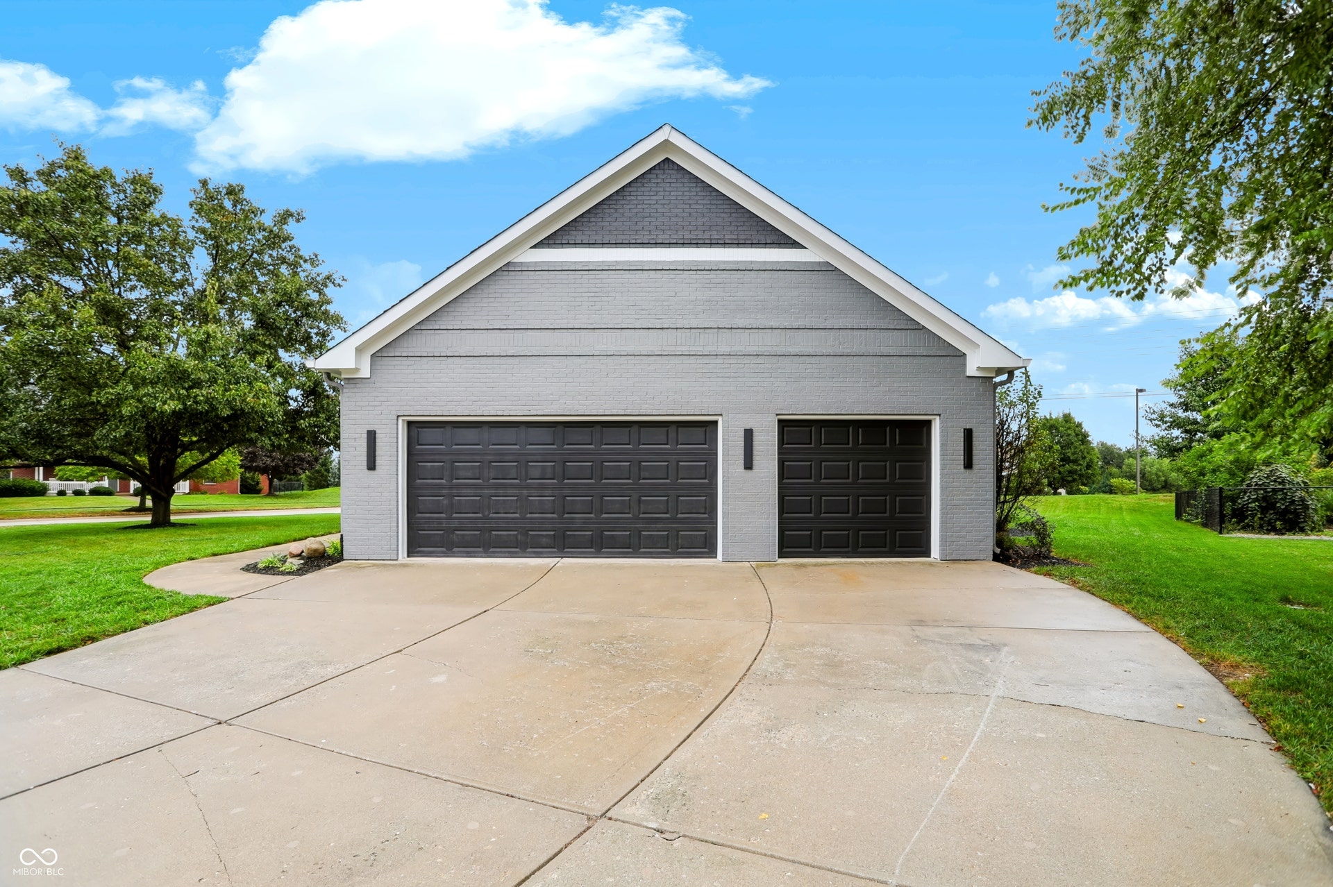 7405 Rooses Drive, Indianapolis, IN 46217 Concrete driveway leading to a three-car garage with dark panels and modern exterior lighting