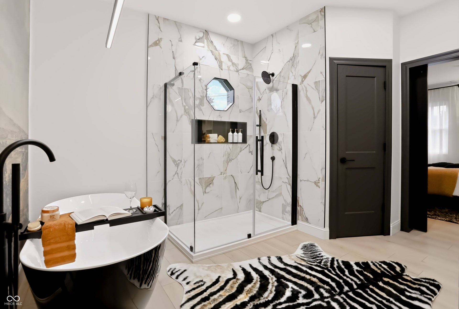 7405 Rooses Drive, Indianapolis, IN 46217 Freestanding black soaking tub, glass-enclosed shower with tiled walls, matte black fixtures, and light wood-finish flooring
