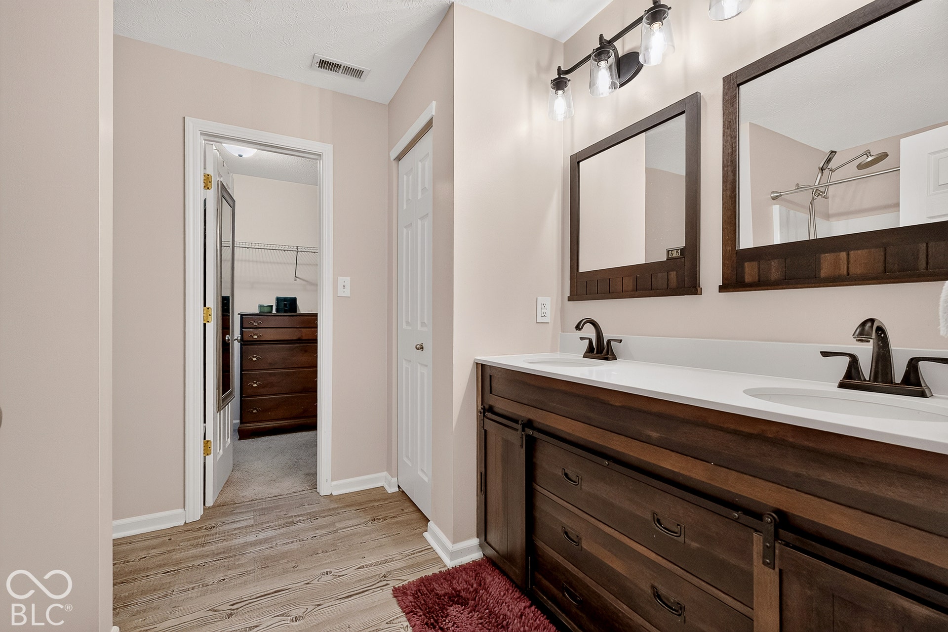 Wood-finish flooring, dual vanity with white countertops, dark wood-finish cabinetry, and framed mirrors