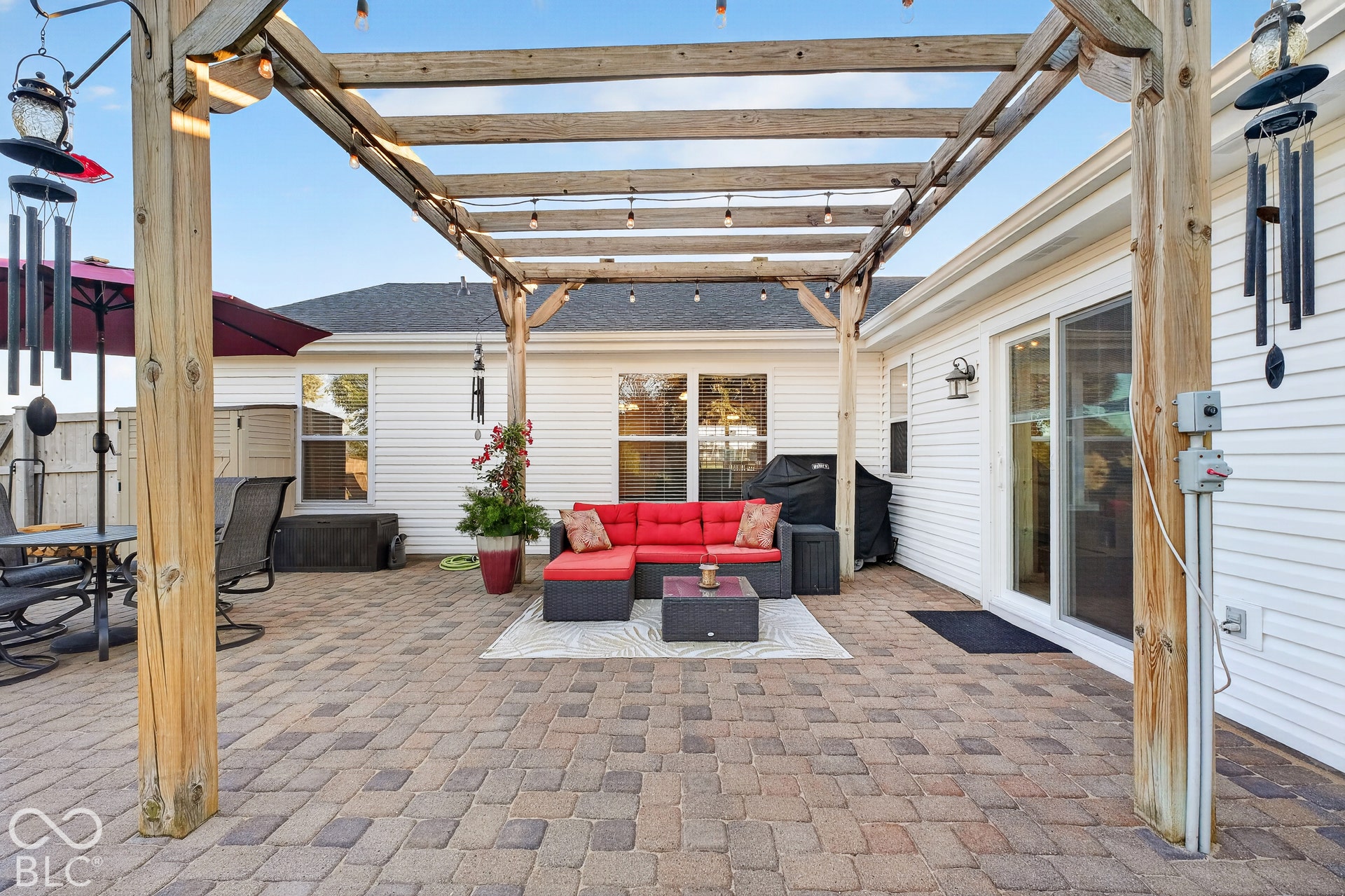 Expansive paver patio with a wood pergola, string lighting, and direct access through a sliding glass door