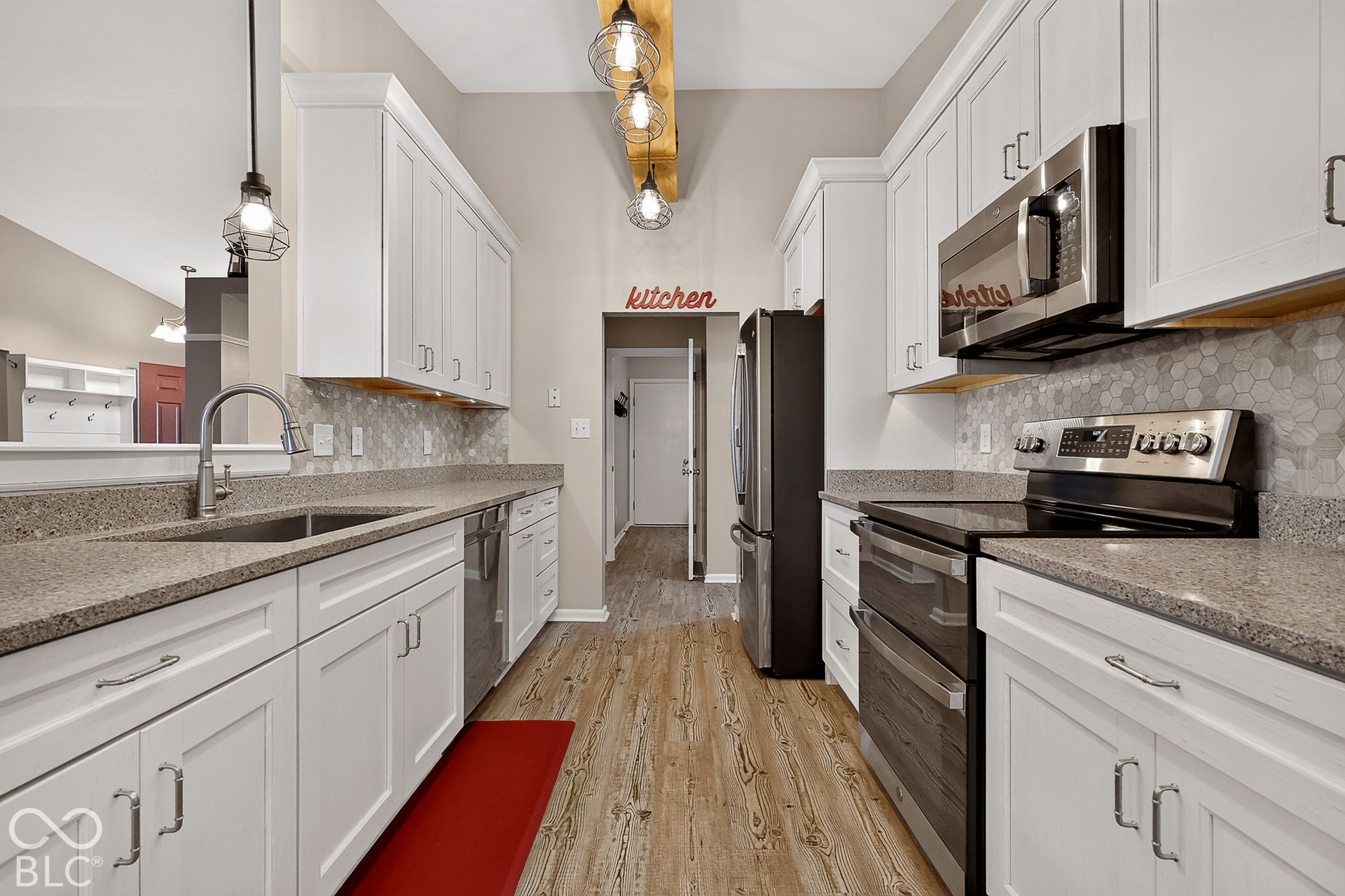 Galley kitchen featuring wood-finish flooring, white cabinetry, integrated stainless steel appliances, and hexagon tile backsplash
