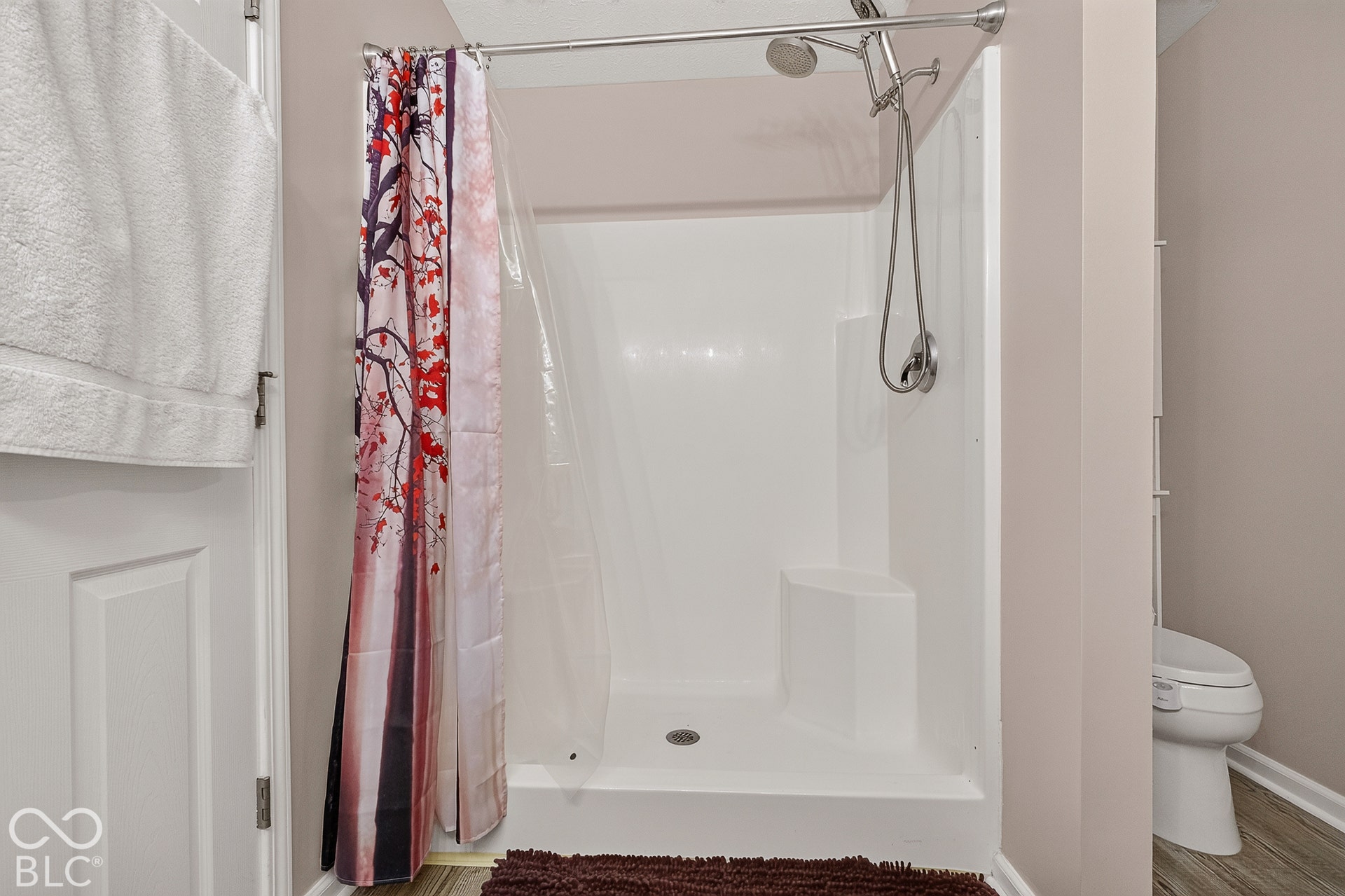 White shower enclosure with a built-in bench, chrome-finish shower head, and gray wood-finish flooring