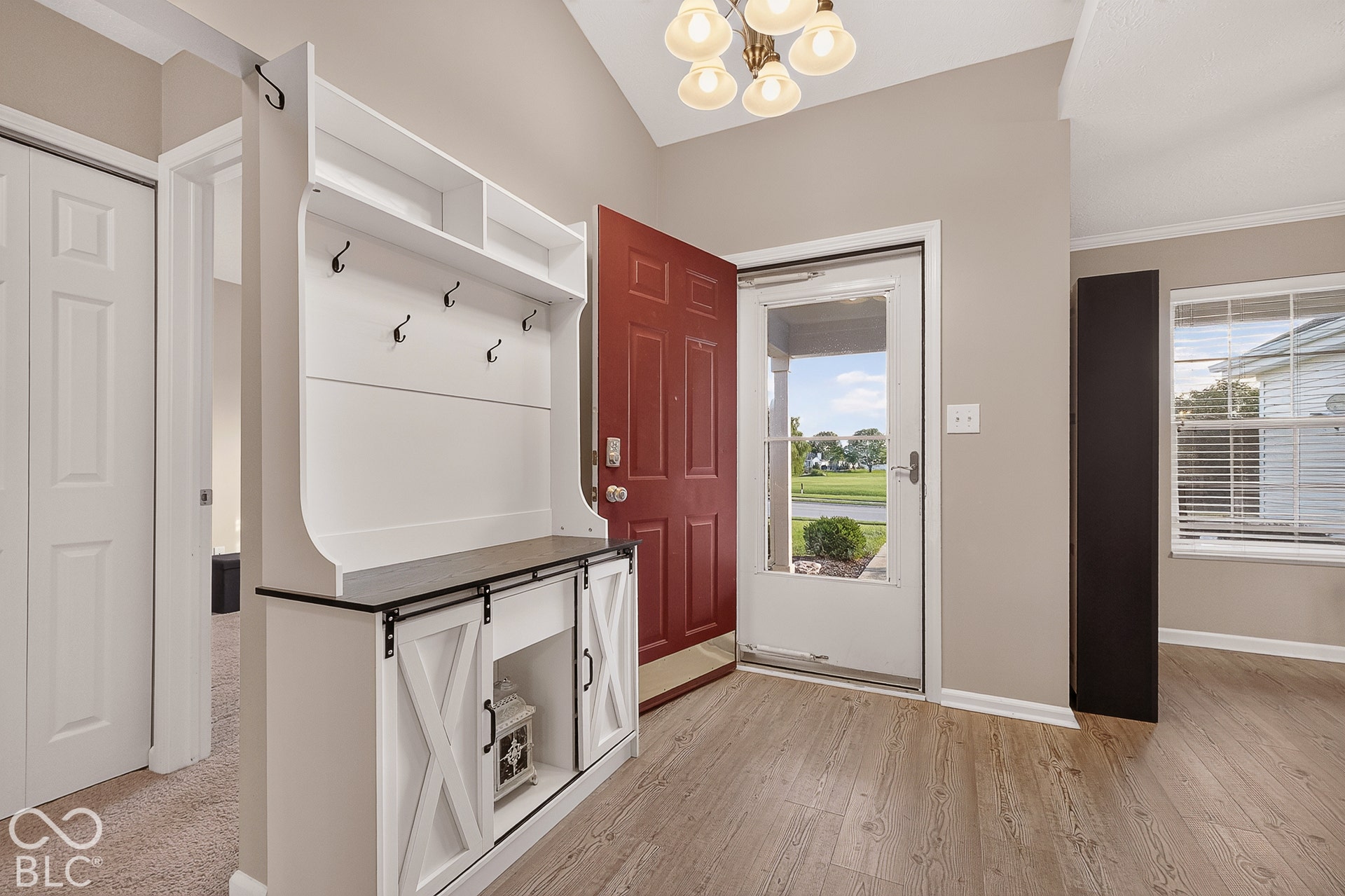 Vaulted ceiling entry with a decorative chandelier, warm wood-finish flooring, and a white built-in storage unit featuring barn-style doors