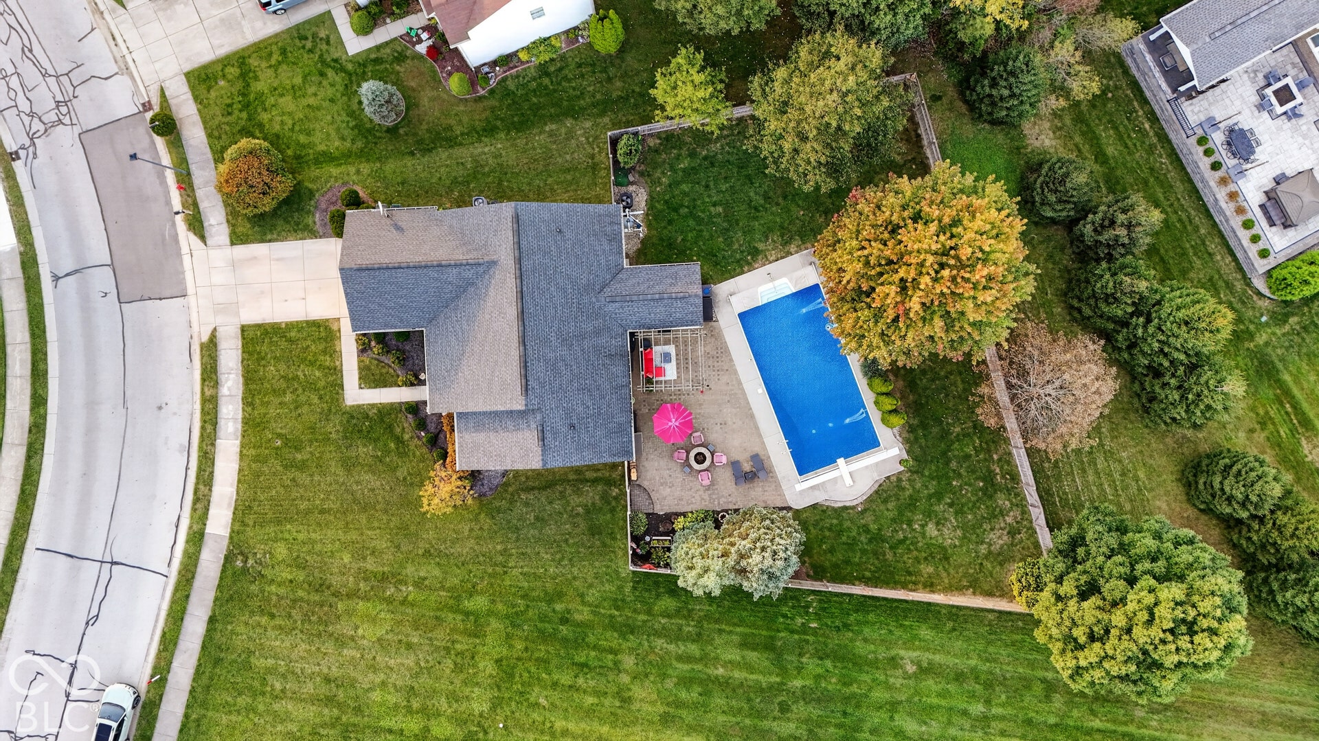 Asphalt shingle roofing, concrete driveway, concrete patio, in-ground swimming pool, and mature landscaping