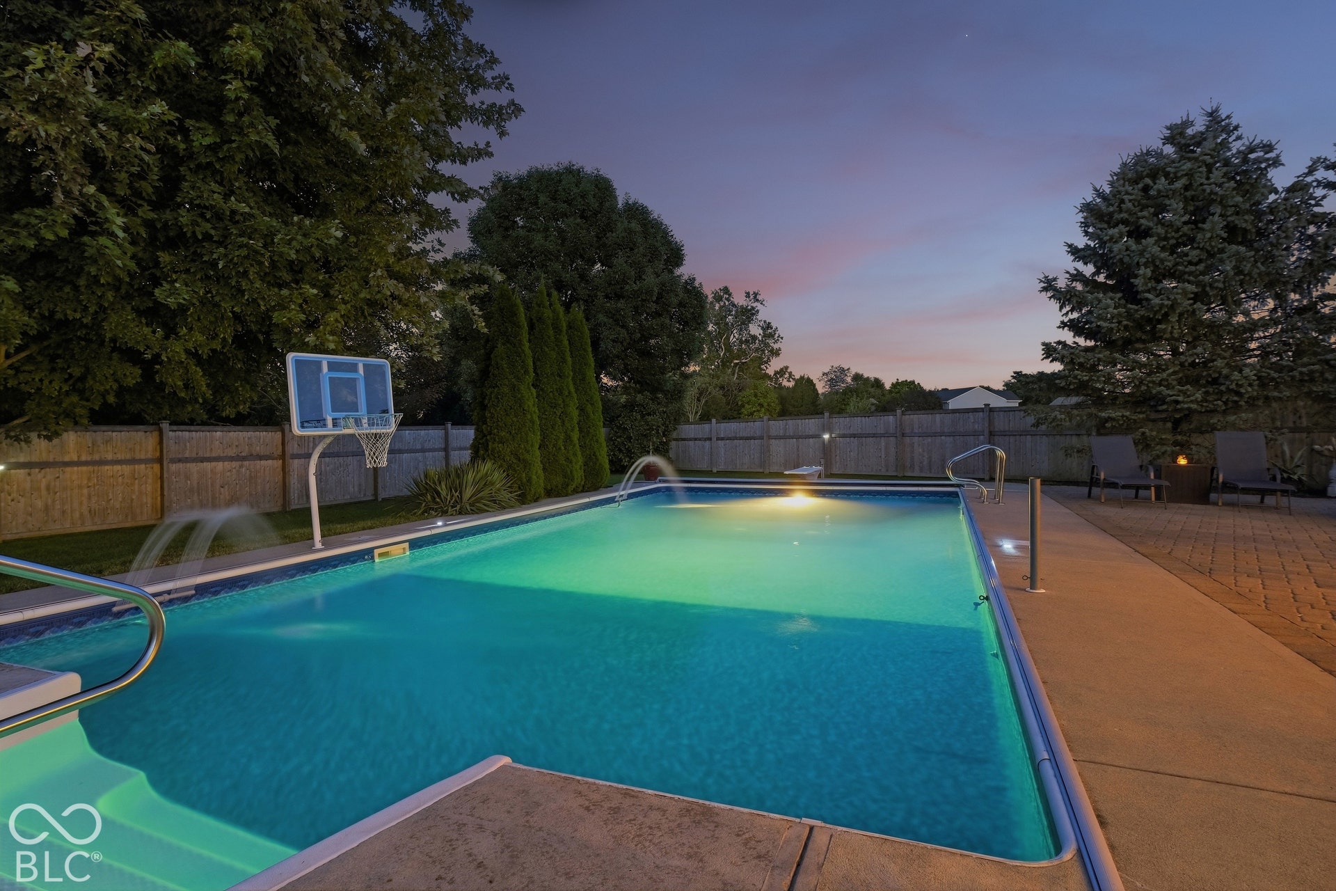 In-ground swimming pool with integrated lighting, water features, and an adjacent paver patio