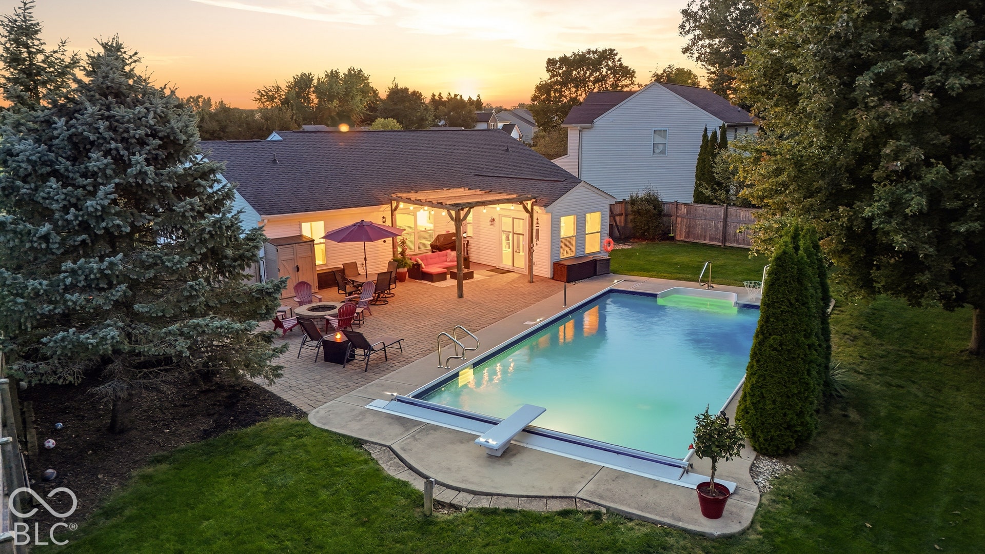 Expansive paver patio with a pergola, built-in fire pit, and inground swimming pool with a diving board