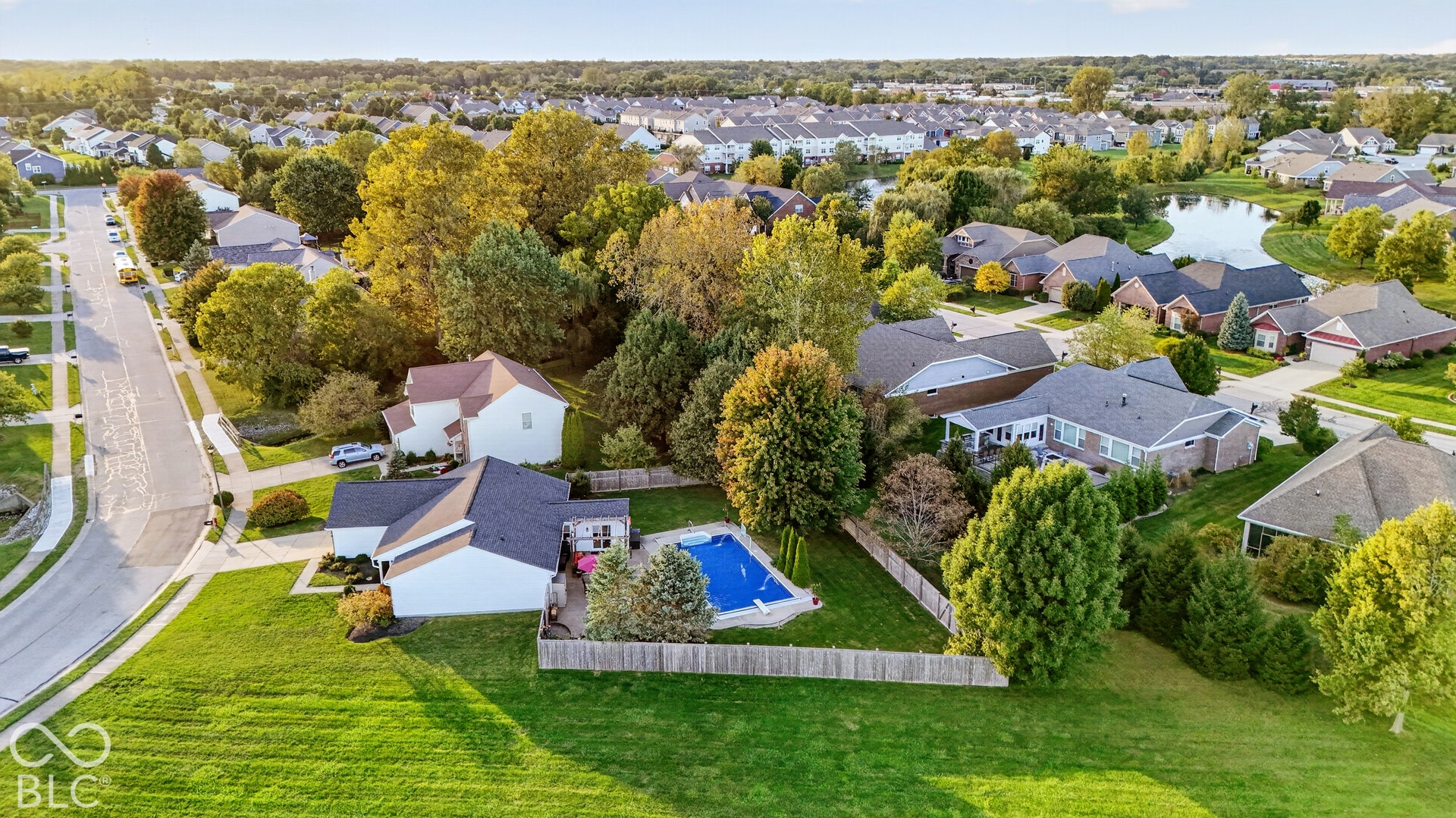 Expansive green lawn with a fenced swimming pool, mature trees, and an extended patio area