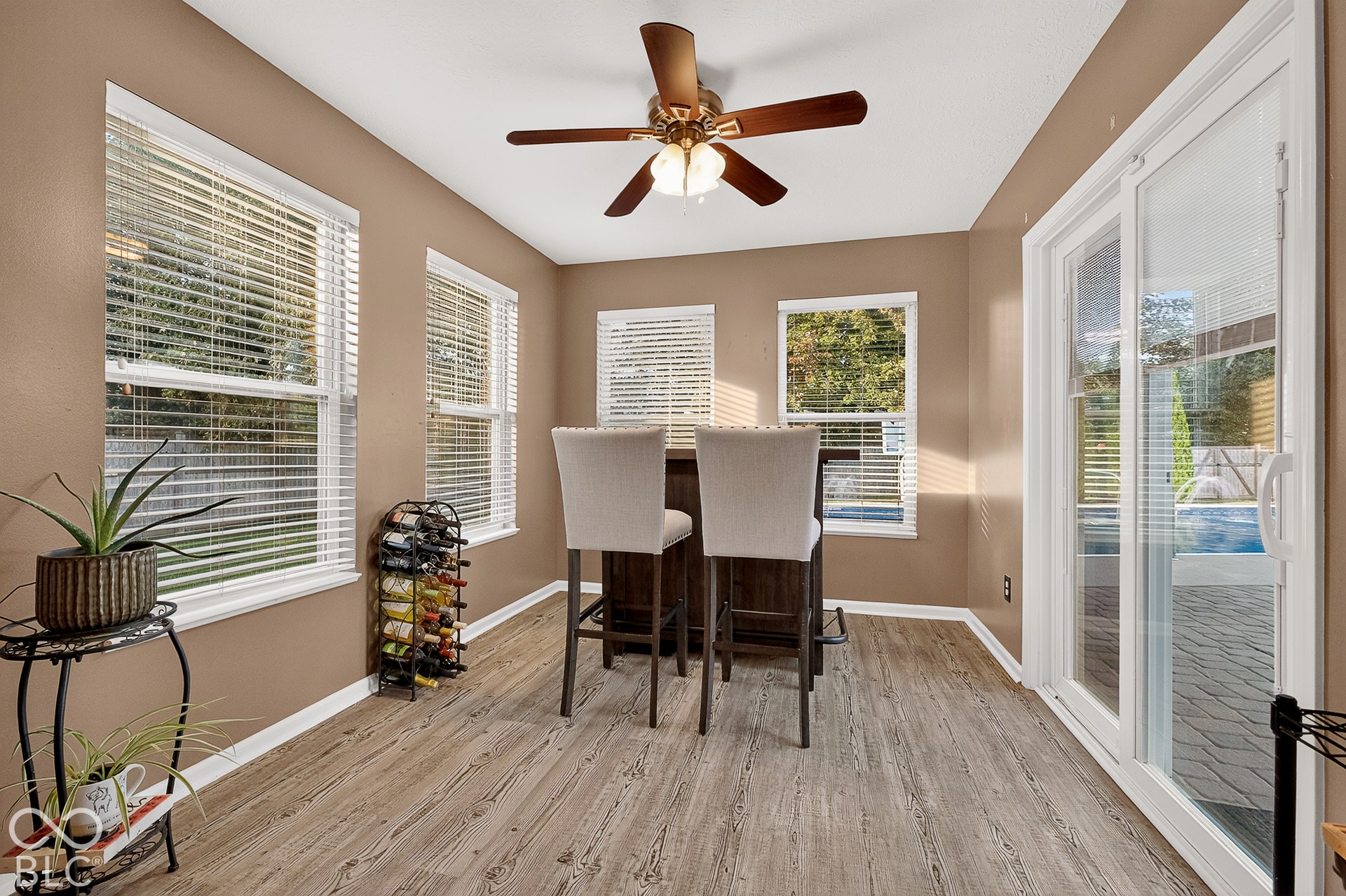 Wood-finish flooring, ceiling fan with integrated lighting, multiple windows, and a sliding glass door