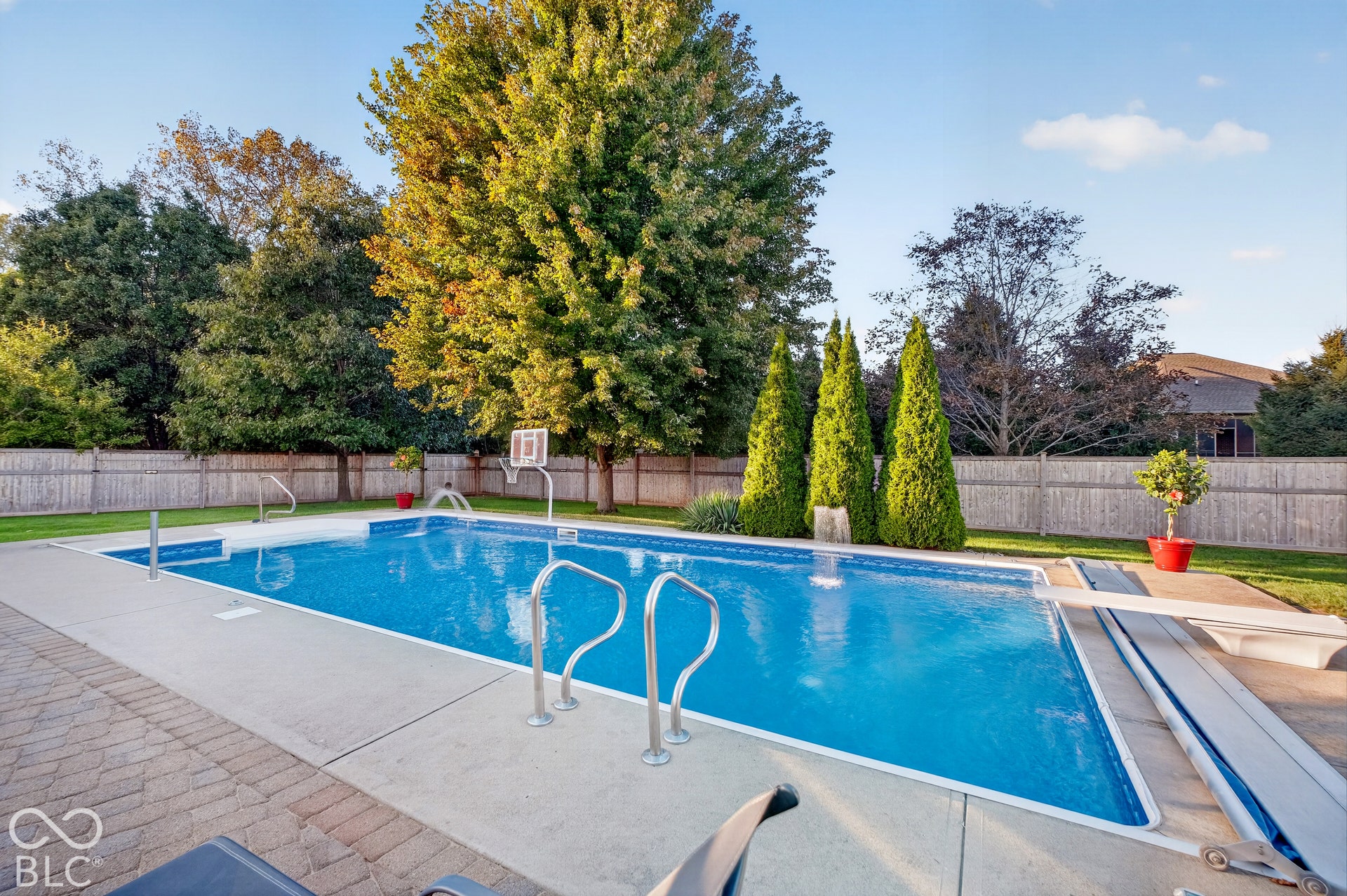 Expansive inground swimming pool with a diving board, surrounding concrete decking, and a paver patio