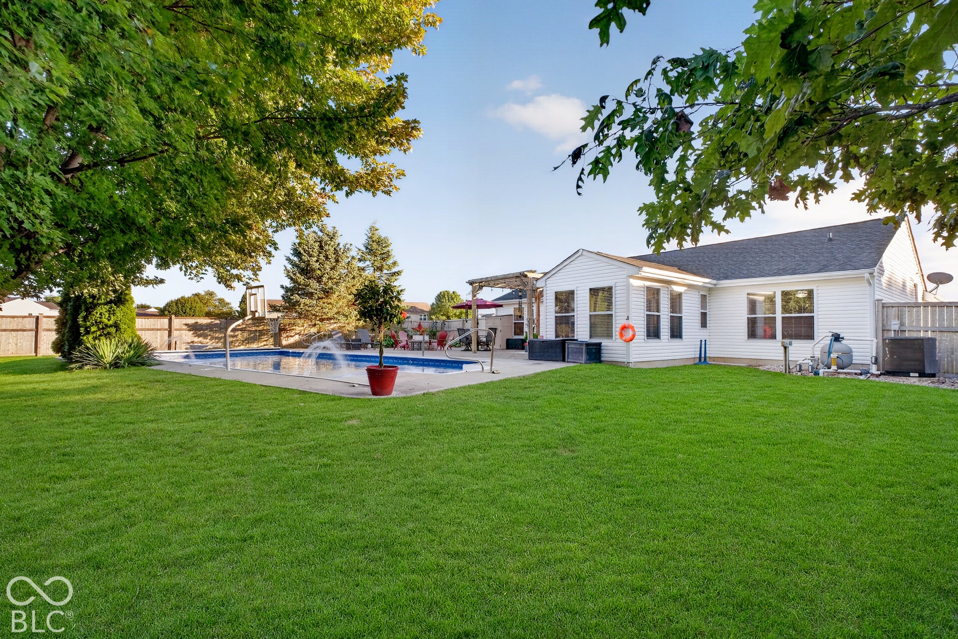 Expansive backyard featuring a manicured lawn, inground swimming pool with water features, and a white siding exterior