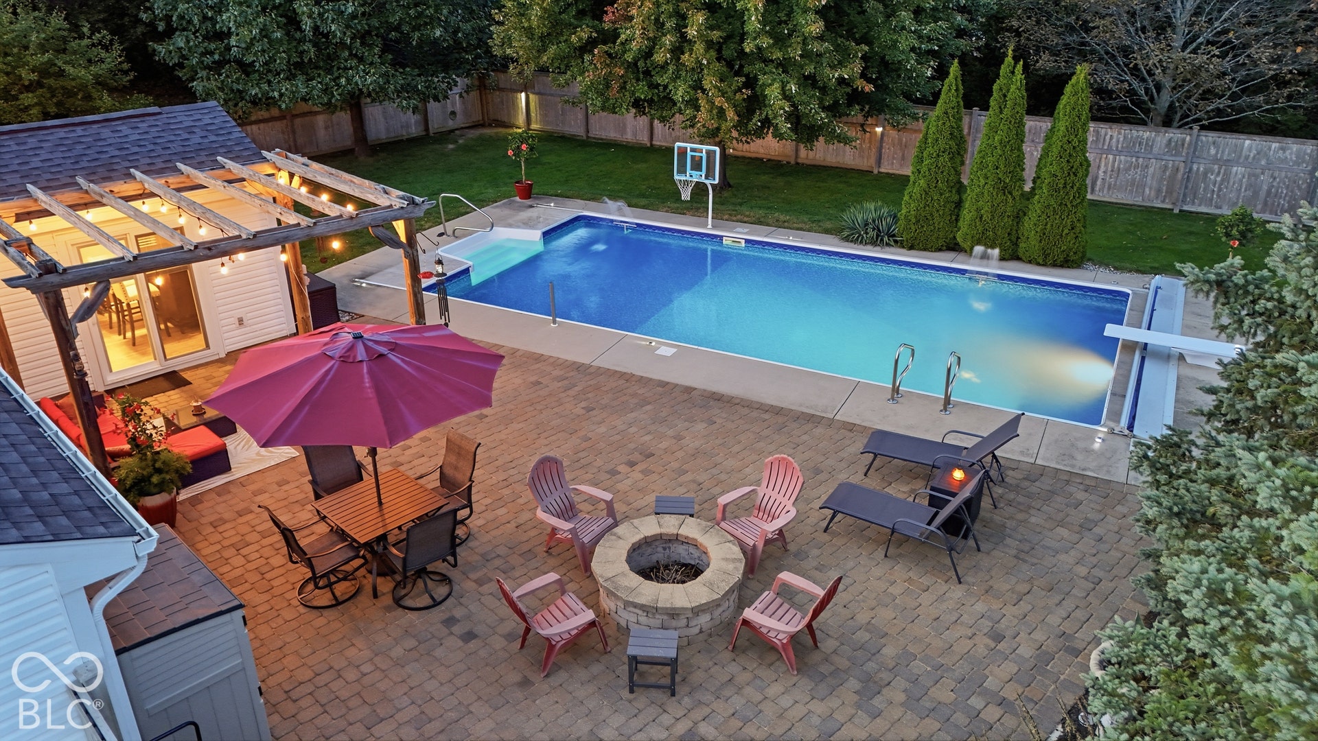 In-ground swimming pool with diving board, extensive paver patio, built-in fire pit, pergola, and manicured lawn