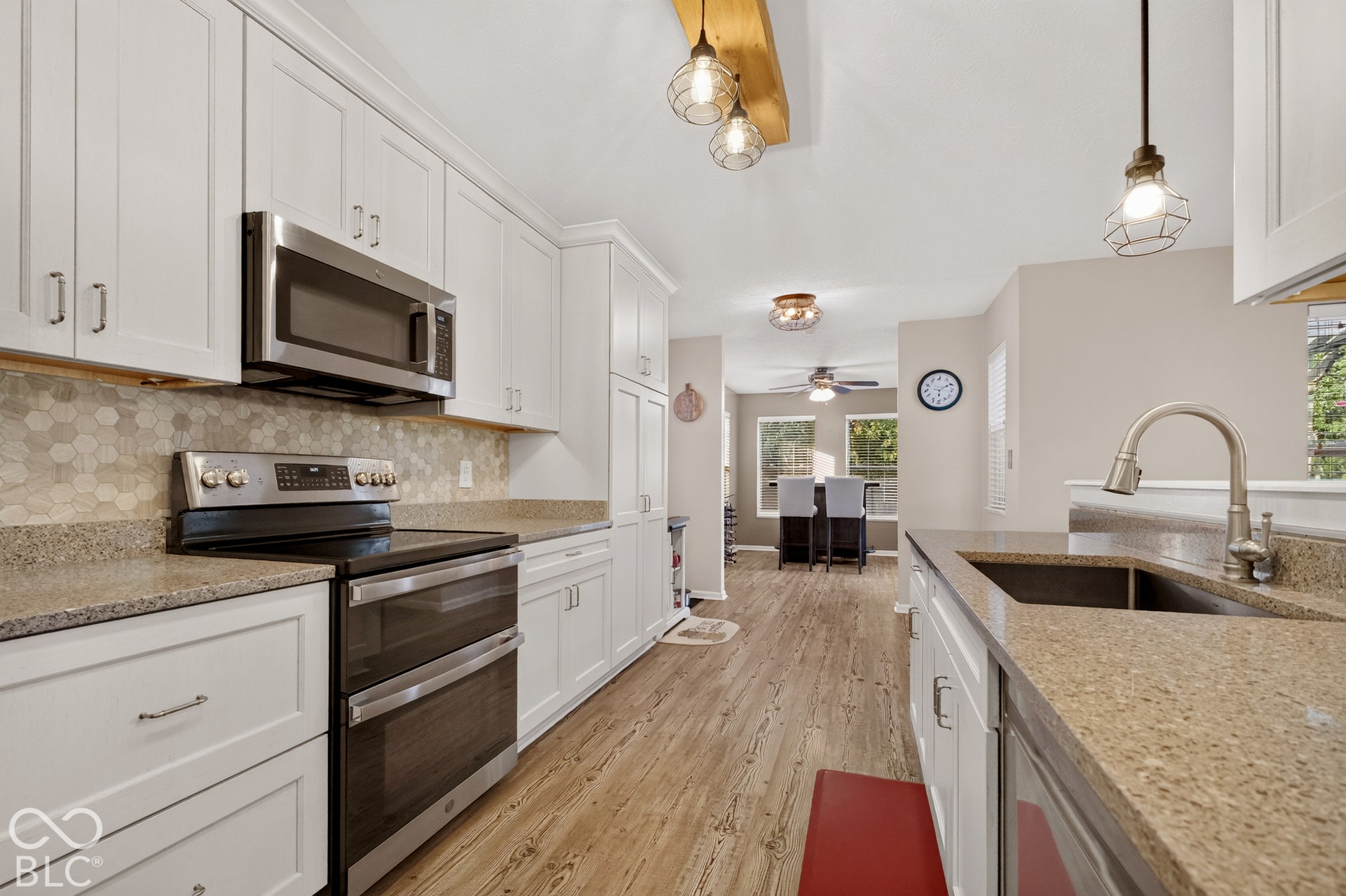 White cabinetry, stainless steel appliances, wood-finish flooring, stone countertops, and a hexagonal tile backsplash