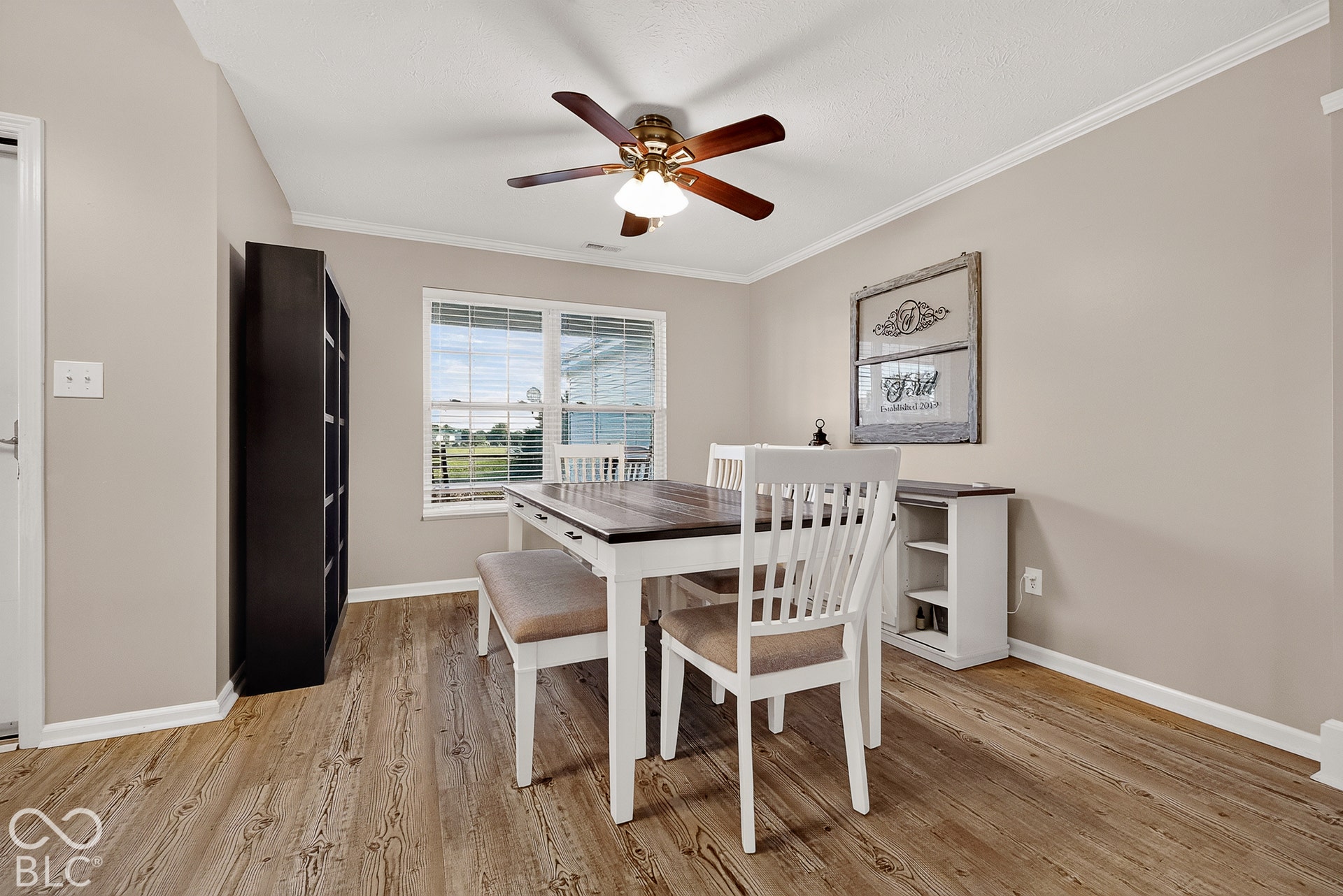 Wood-finish flooring, ceiling fan with light fixture, double window with blinds, crown molding, and baseboards