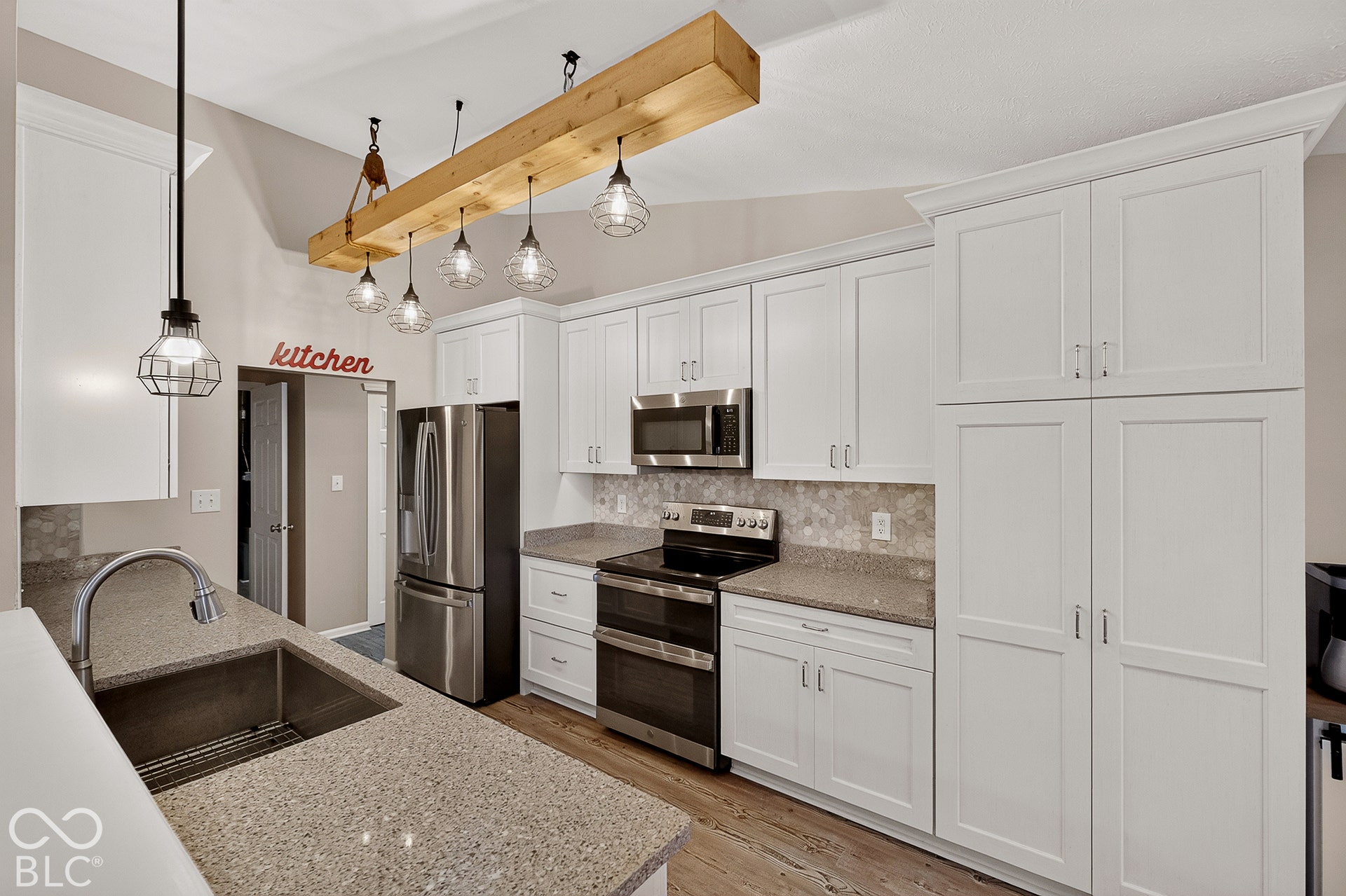 White shaker cabinetry, stainless steel appliances, stone countertops, undermount sink, and wood-finish flooring