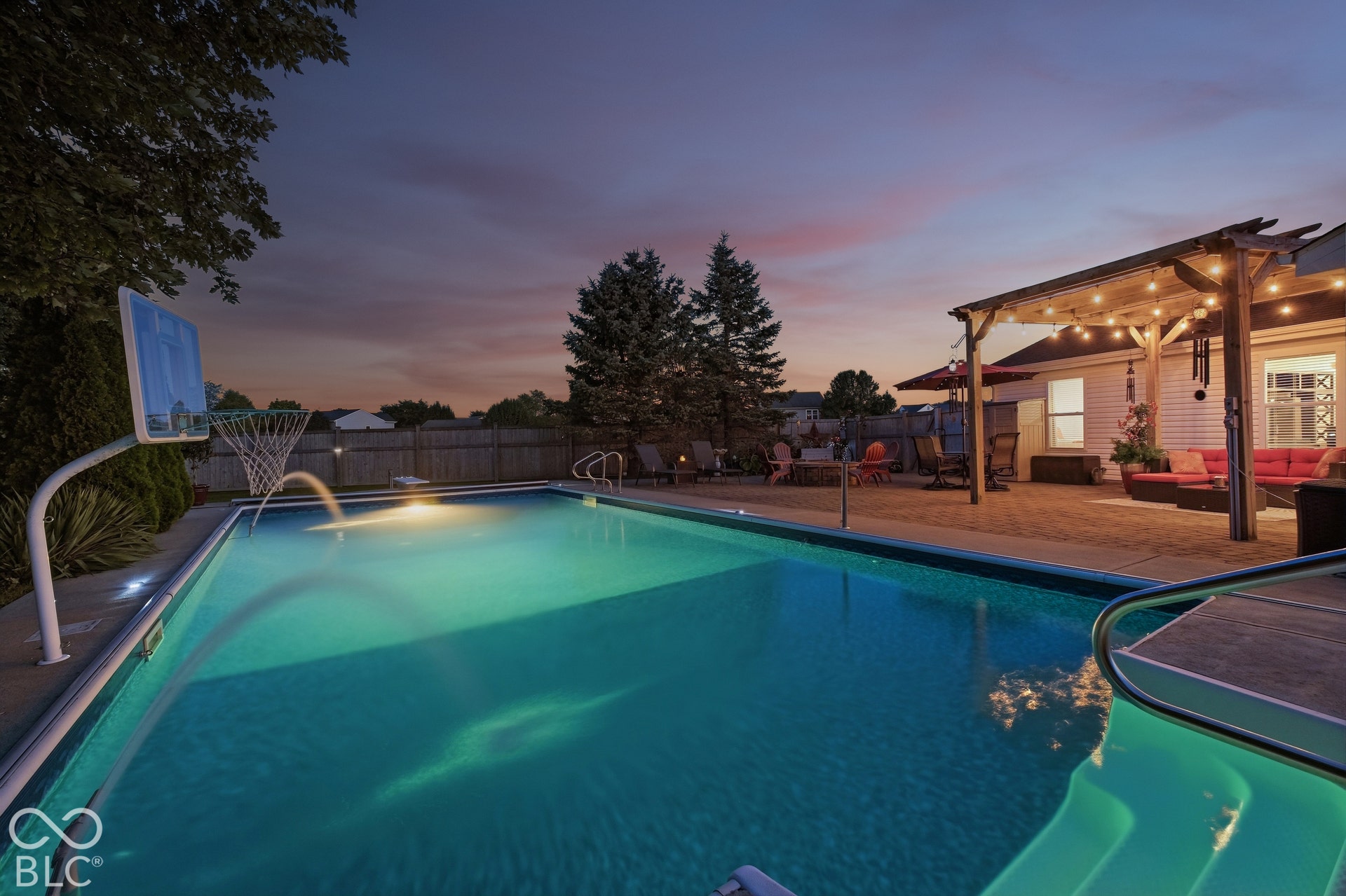 Expansive backyard featuring an in-ground swimming pool, a basketball hoop, and a paved patio area
